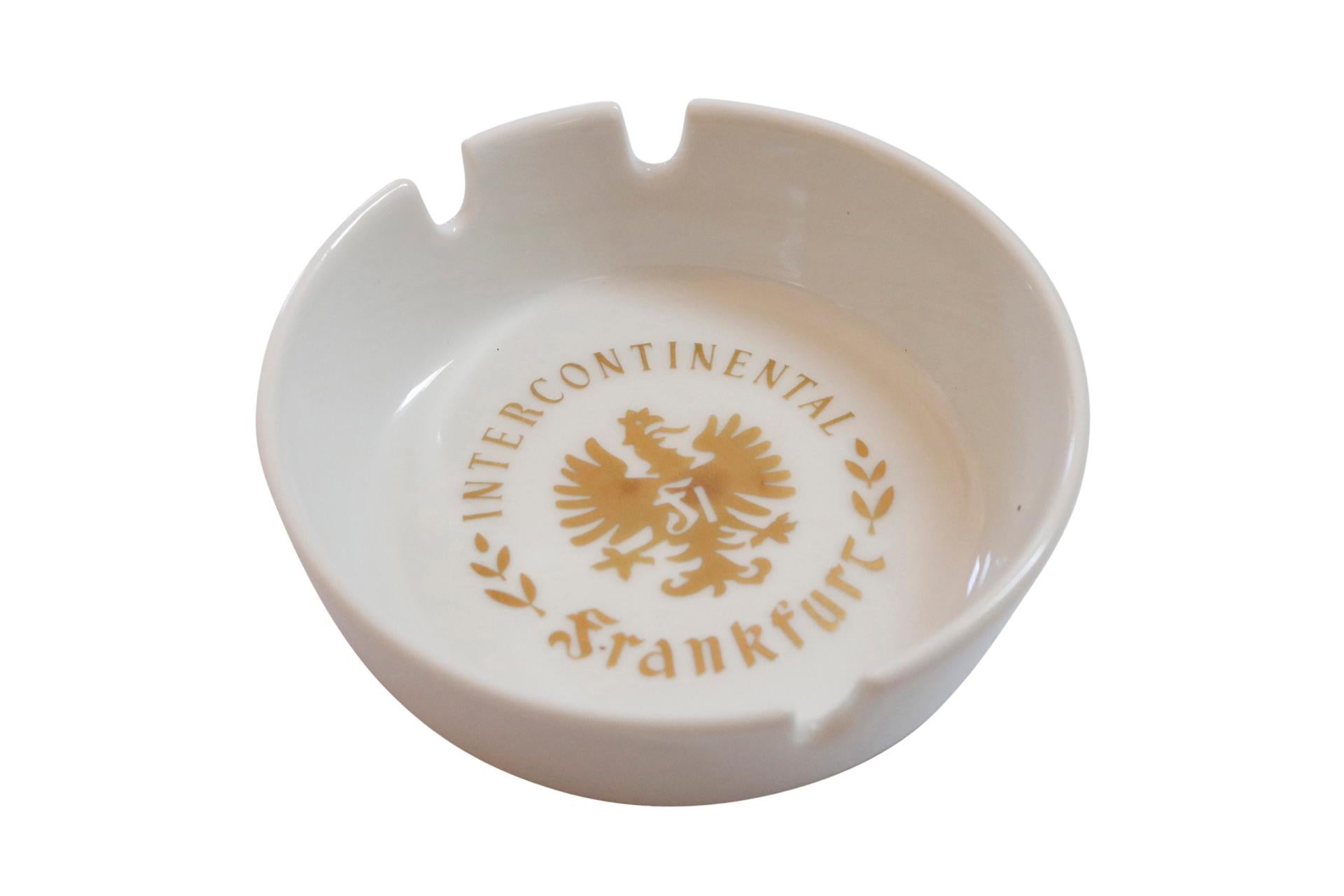 A cream ceramic ashtray from the Intercontinental Hotel in Frankfurt, Germany. The center is printed with the Intercontinental Hotel logo in gold. Marked underneath Schönwold, Germany. Hotel Intercontinental Frankfurt/Deutschland. 