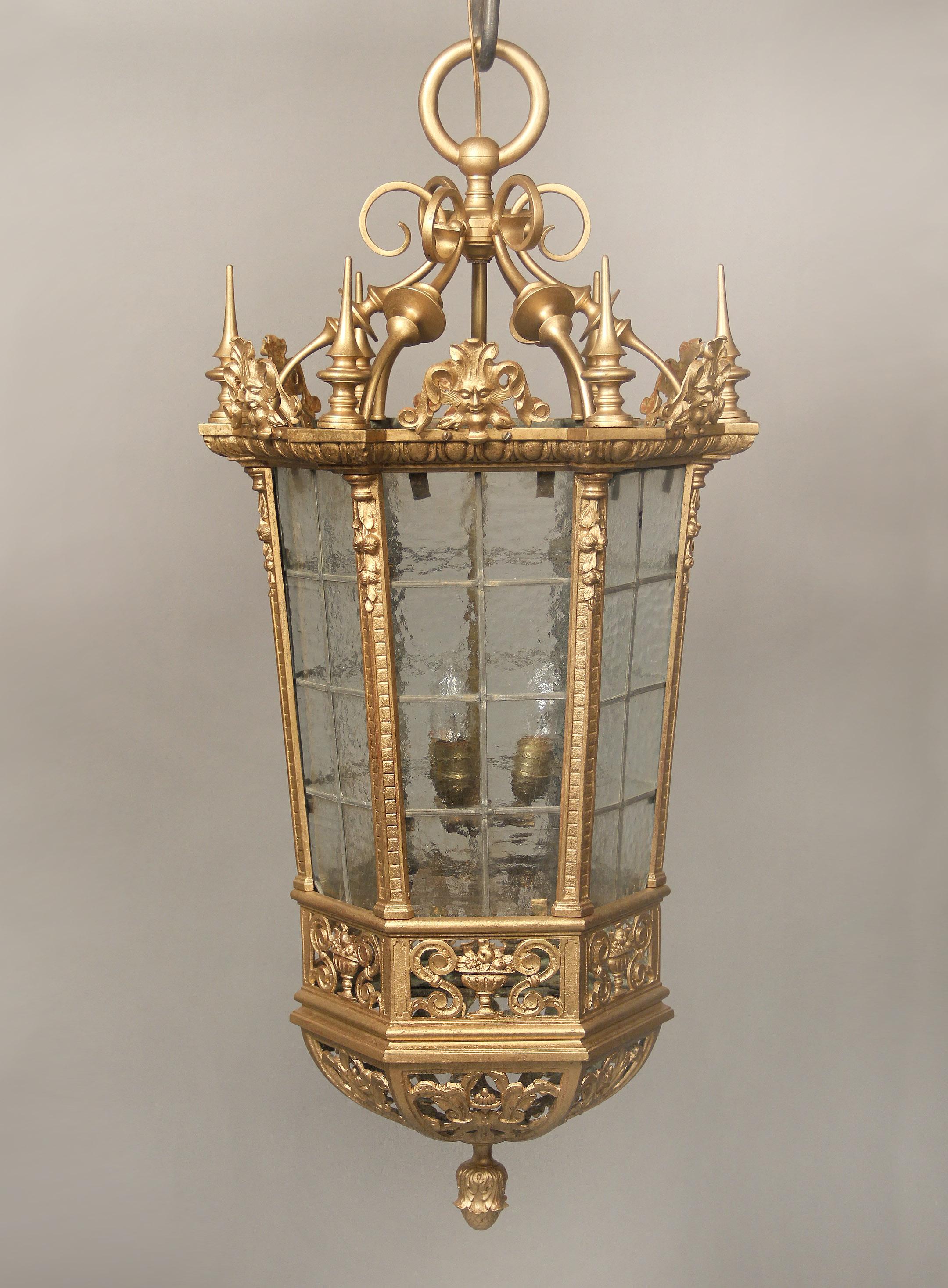 An interesting late 19th century gilt bronze and rippled glass Gothic lantern.

The bronze top with six male masks with pointed spears on each corner, above a hexagonal shaped body with designs of floral and fruit bouquets and the bottom finished