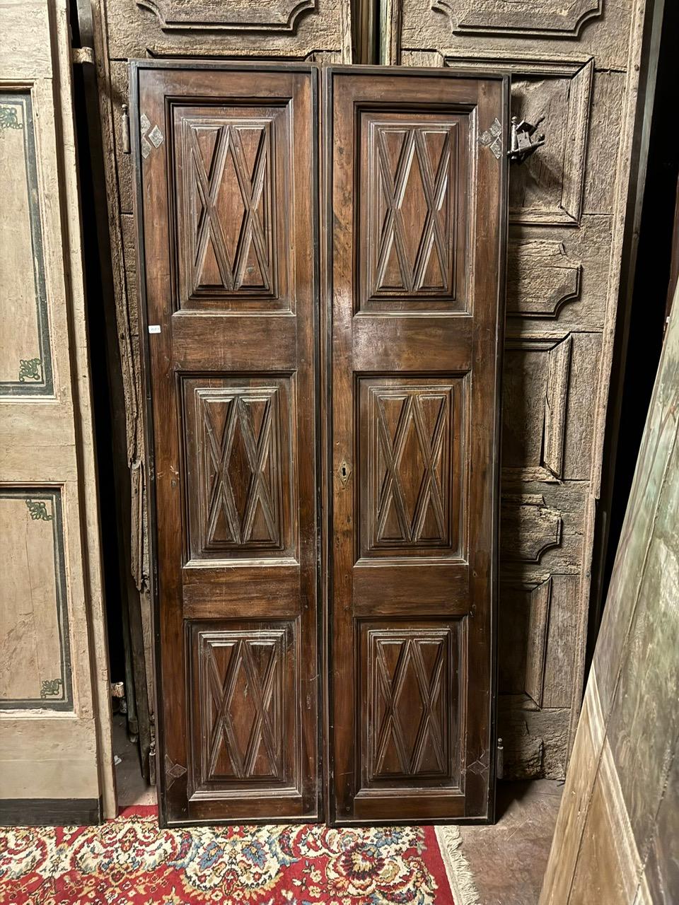 Antique double-leaf walnut interior door, richly carved panels with geometric shapes, smooth back but where the hand-crafted wood cutting is visible, complete with original wall irons (hinges). The door has a pull opening, without a frame, it was