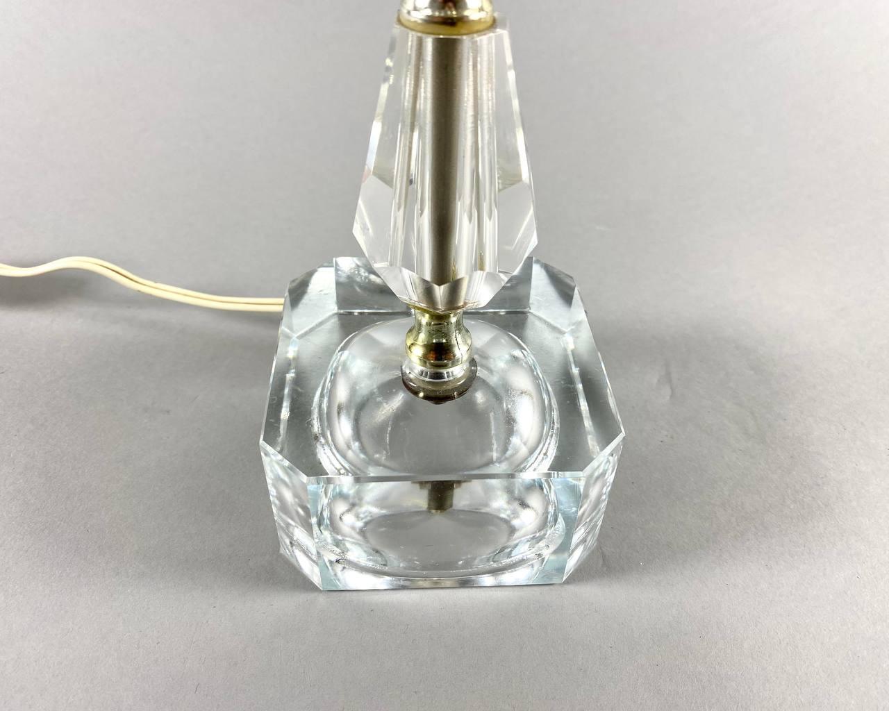 This vintage table lamp has a simple design with a minimal amount of decorative elements. 

Massive details made of transparent faceted glass are fixed on thin bronze-colored metal fittings. 

The lampshade is new, covered with a cream-colored