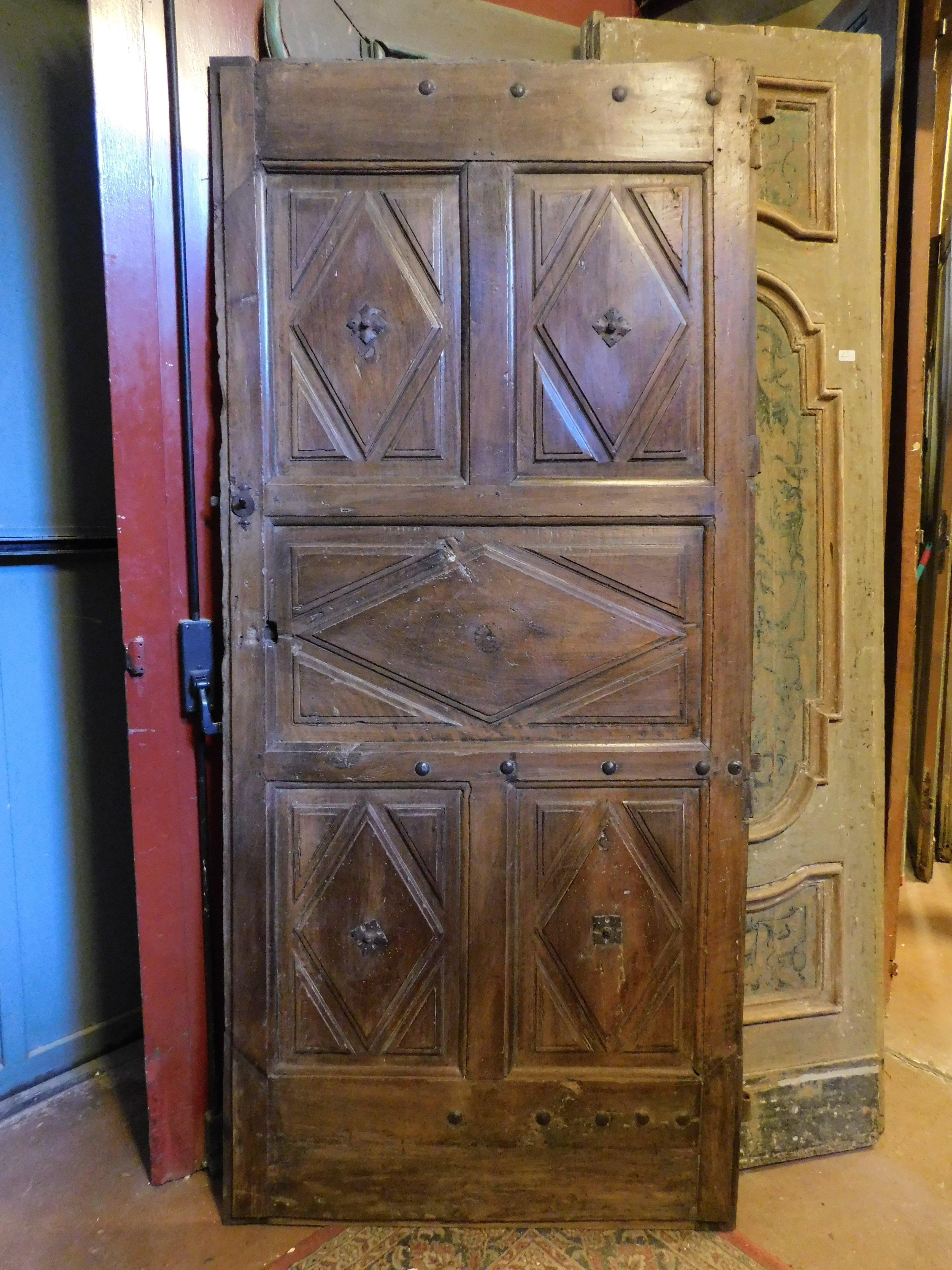 Ancienne porte intérieure en bois, porte simple avec panneaux sculptés à la main avec des carreaux en forme de losange, en bois précieux de noyer massif patiné, du Piémont (Italie), des années 1600, dos lisse, ouverture par poussée vers la droite,
