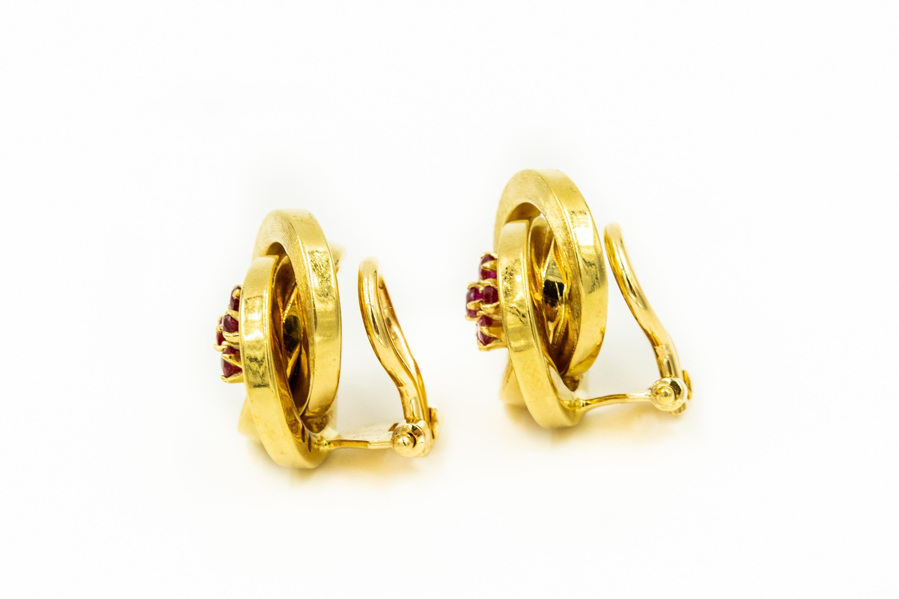 Beautifully made three dimensional Italian clip-on earrings featuring 3 interlocking round rings that swirl around a ruby center that resembles a flower.  The earrings are 18k yellow gold with a Florentine matte finish.  The earrings have a lever