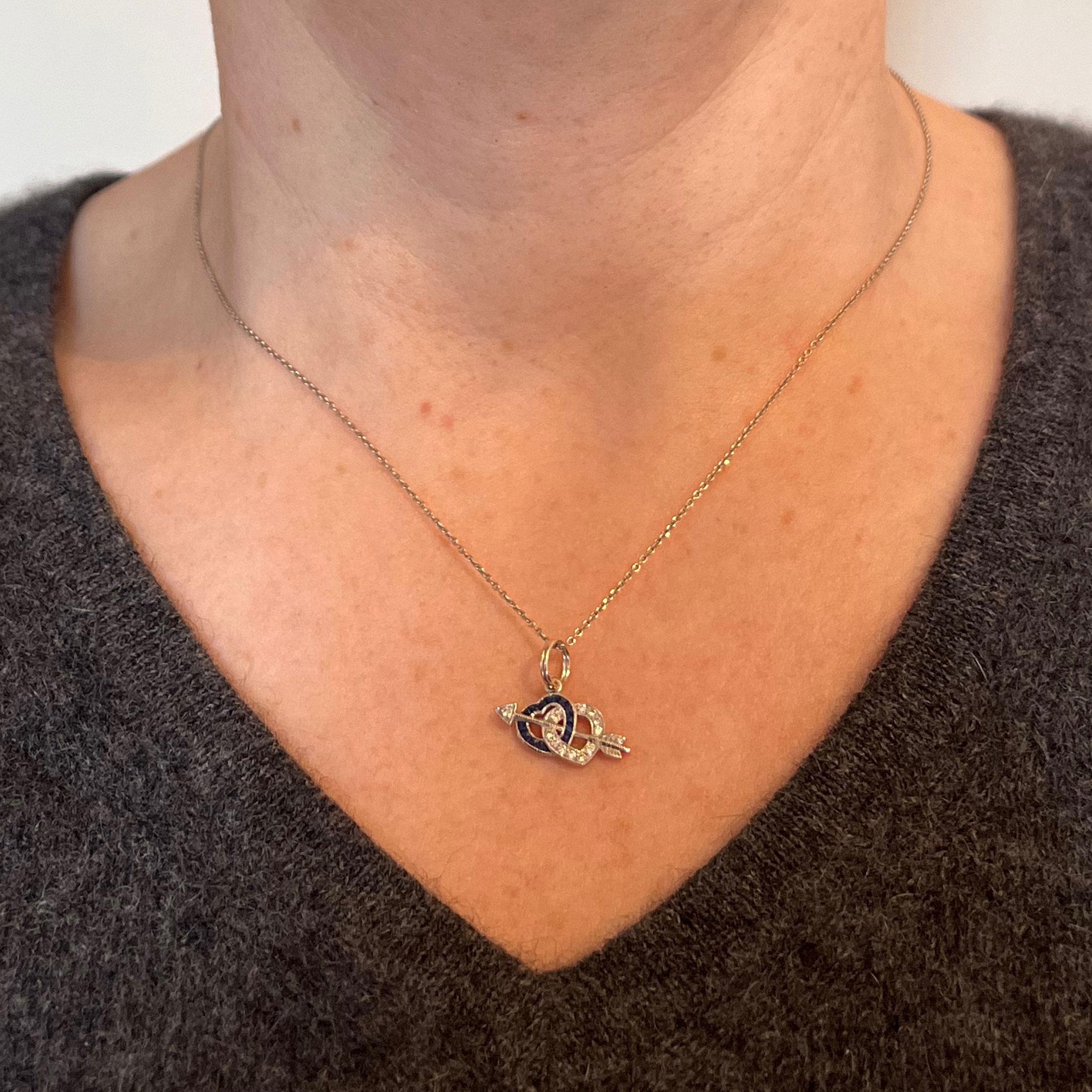 A platinum charm pendant designed as a pair of interlocking hearts in white diamonds and blue sapphires, connected by Cupid’s arrow. Set with 12 round brilliant cut white diamonds and 13 French cut blue sapphires in unmarked but tested