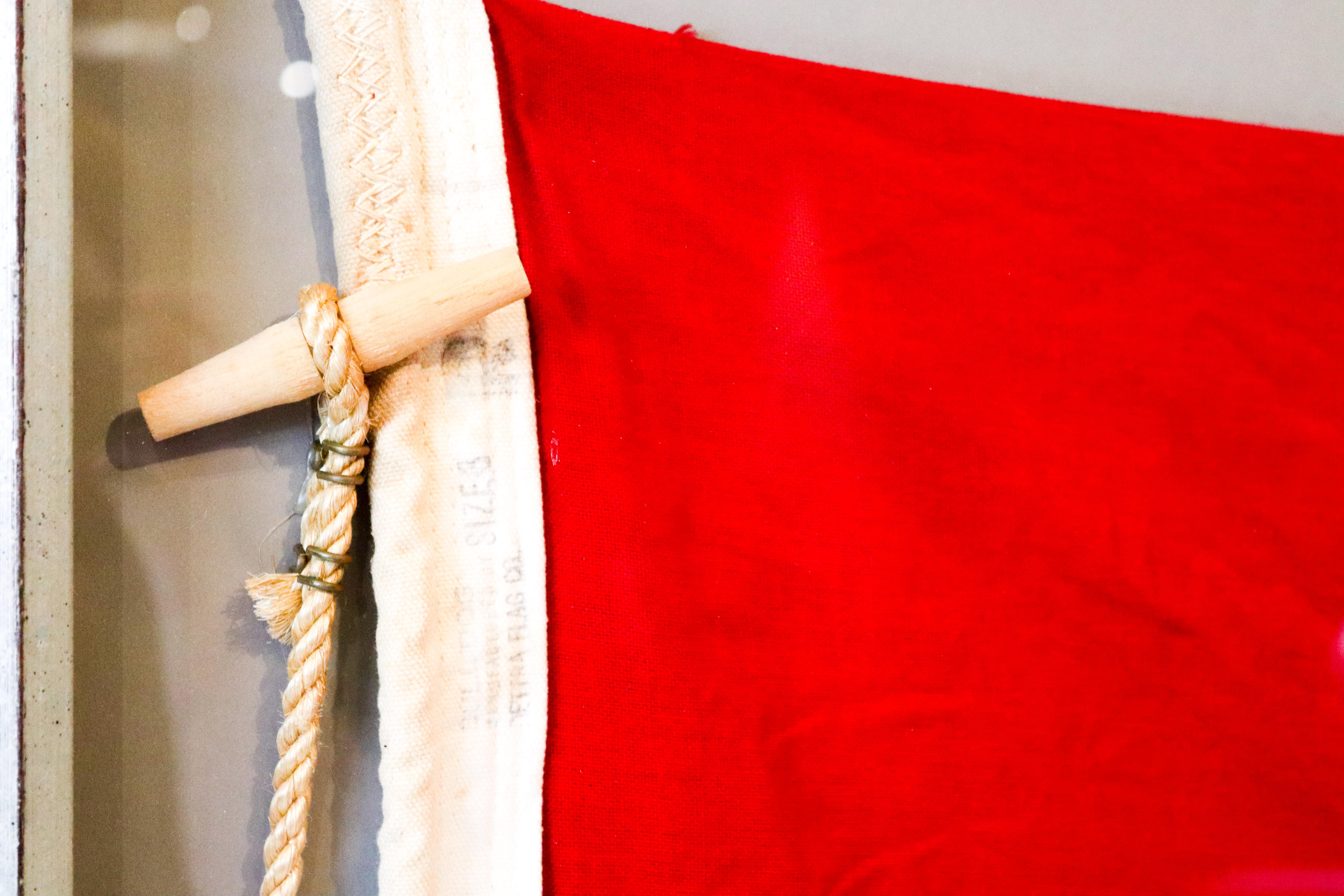 International code of signals maritime flag in shadowbox frame with manila rope and wood toggle. Red field with yellow centre cross represent the letter 