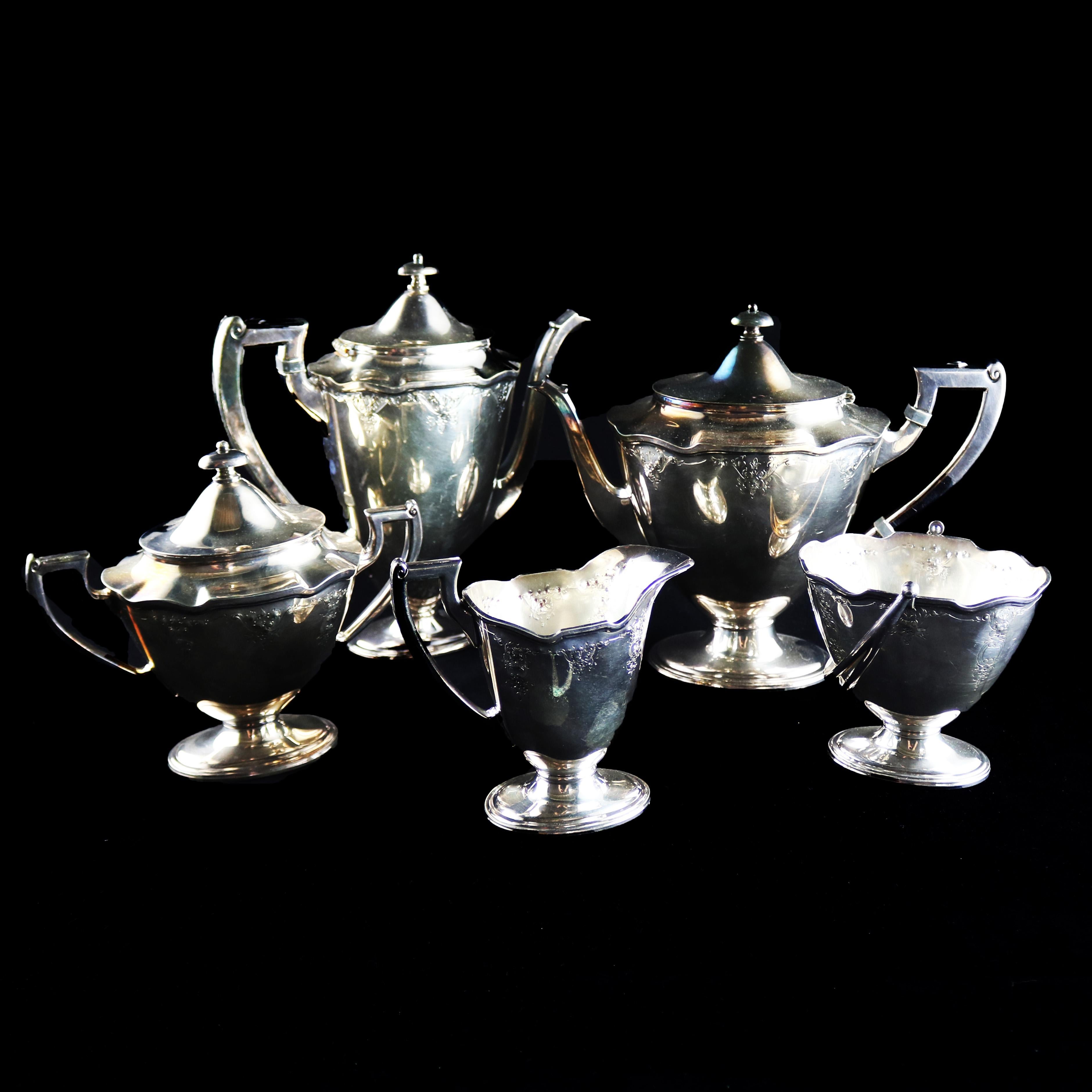 A silver plate coffee and tea set by International Silver Co. offers urn form English Regency styling with floral decoration and includes coffee pot, tea pot, creamer, lidded sugar and handled waste, all with ruffled rims and footed on pedestals,