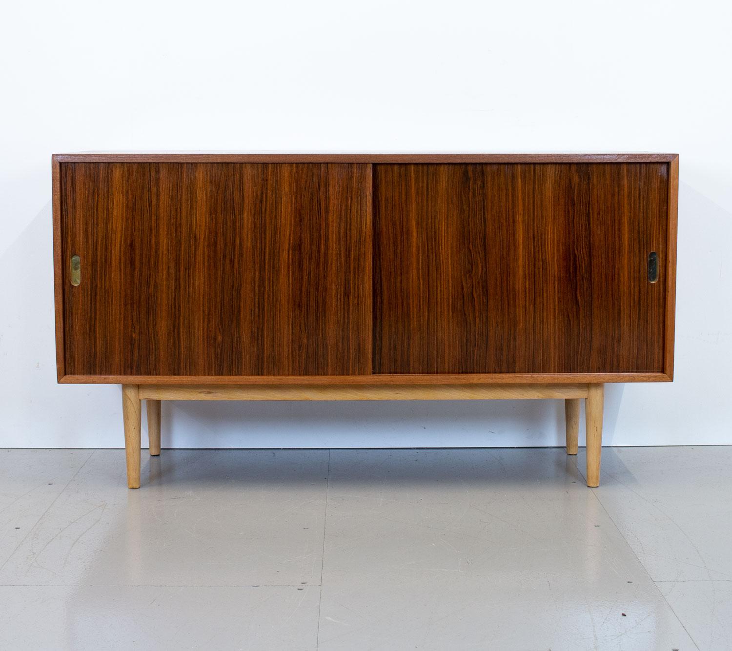 Unit ‘K’ sideboard designed by Robin Day as part of the Interplan range for Hille in 1954. It has a mahogany frame, rosewood sliding doors, beech legs and recessed brass handles. The interior contains 2 adjustable shelves one which has a cutaway