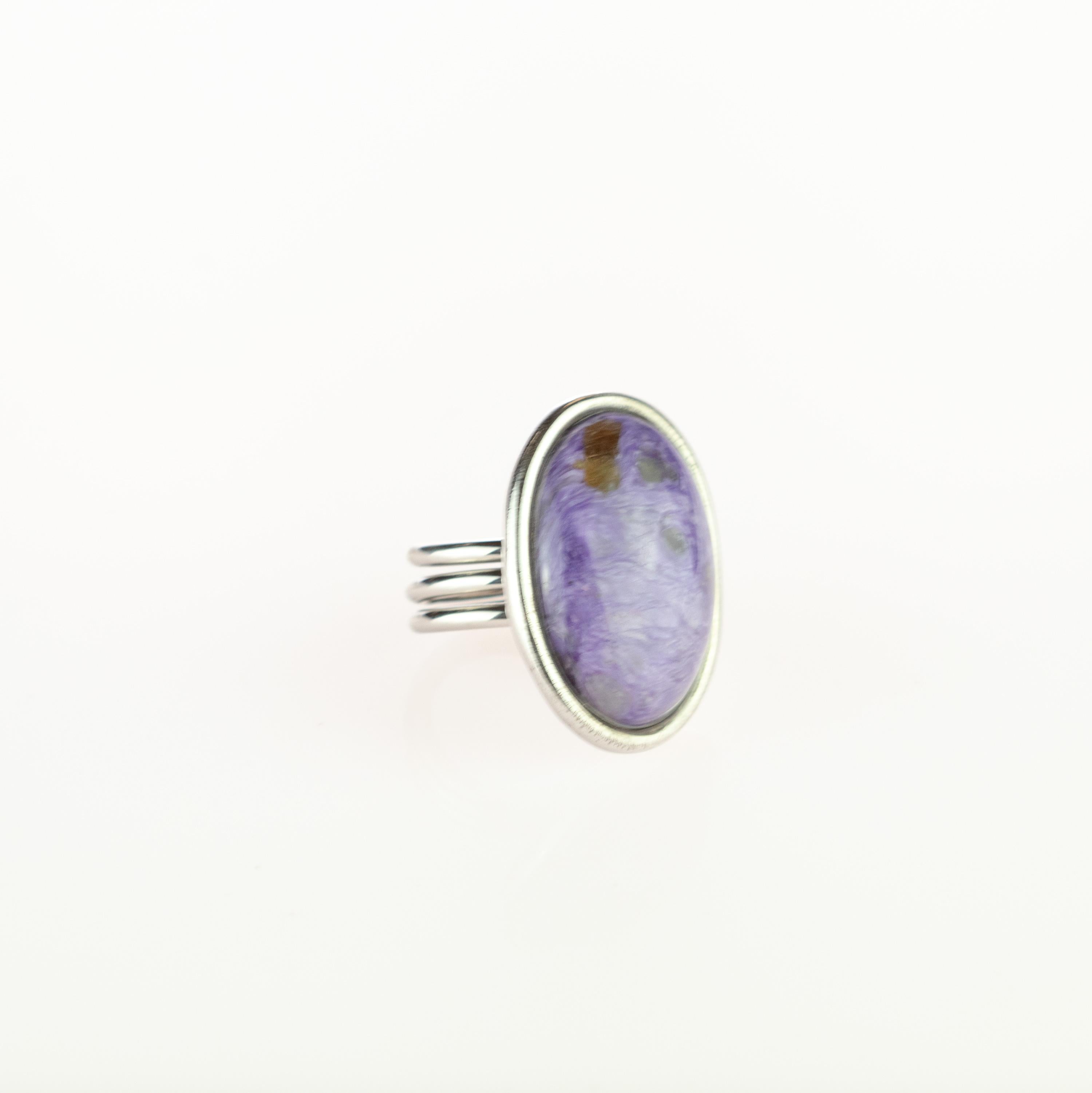 Pietra preziosa di charoite viola incastonata in un gioiello dal design moderno. Una maestosa gemma circondata da argento sterling 925 trattenuta da 3 strisce. Un semplice ma squisito design solitario di un anello cocktail con cabochon ovale che