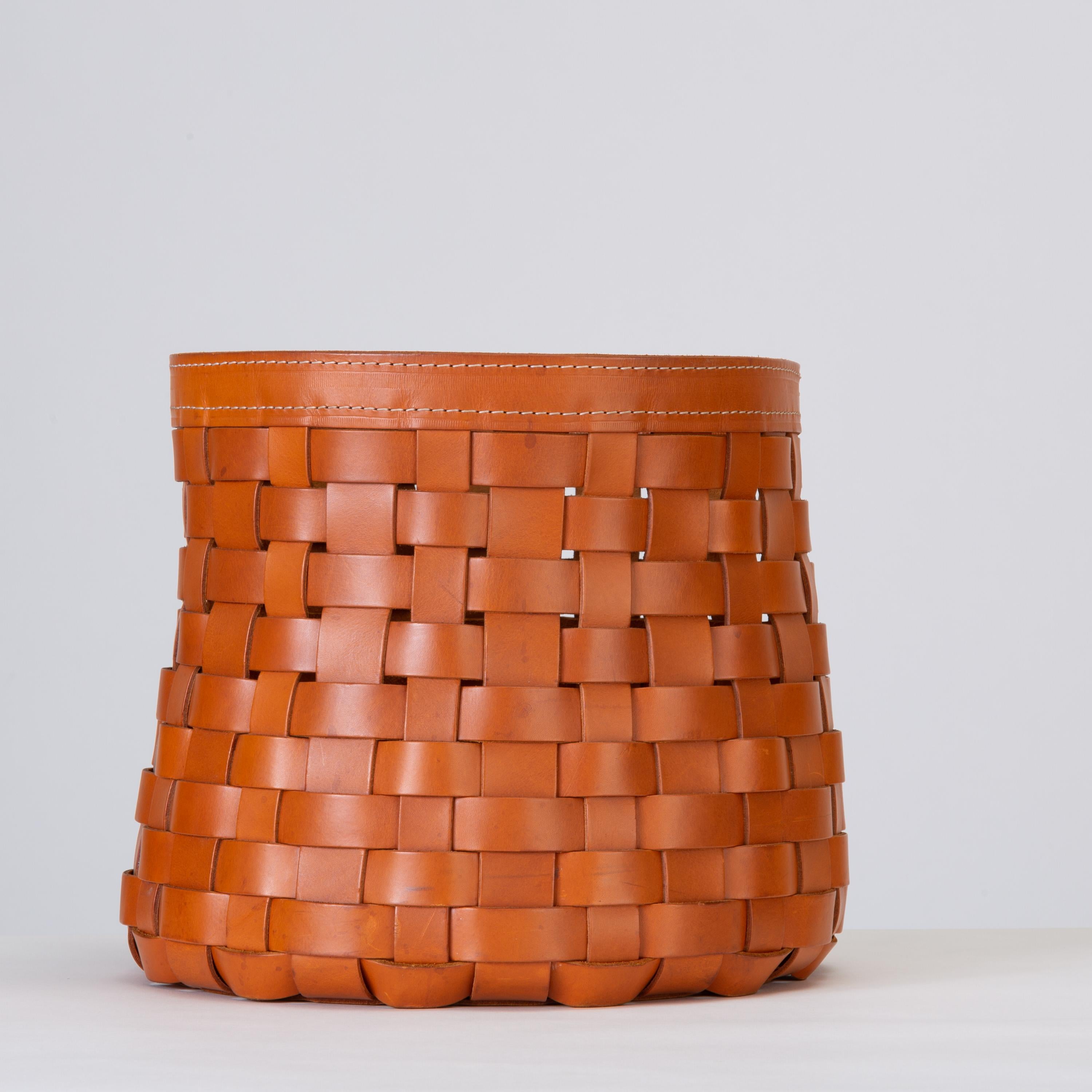 An Italian-made decorative basket or storage vessel by Arte Cuoio e Triangolo. The rounded piece widens towards the reinforced foot, with a thick band of matching leather around the lip. The basket weave of the leather pays homage to a time-honored