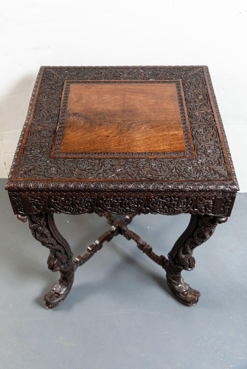 Striking, all-over-carving, Anglo-Indian, hardwood side table featuring beautifully rendered dragon feet between a serpentine X-stretcher. The whole embellished with foliate, reptile scale, and animal motifs.