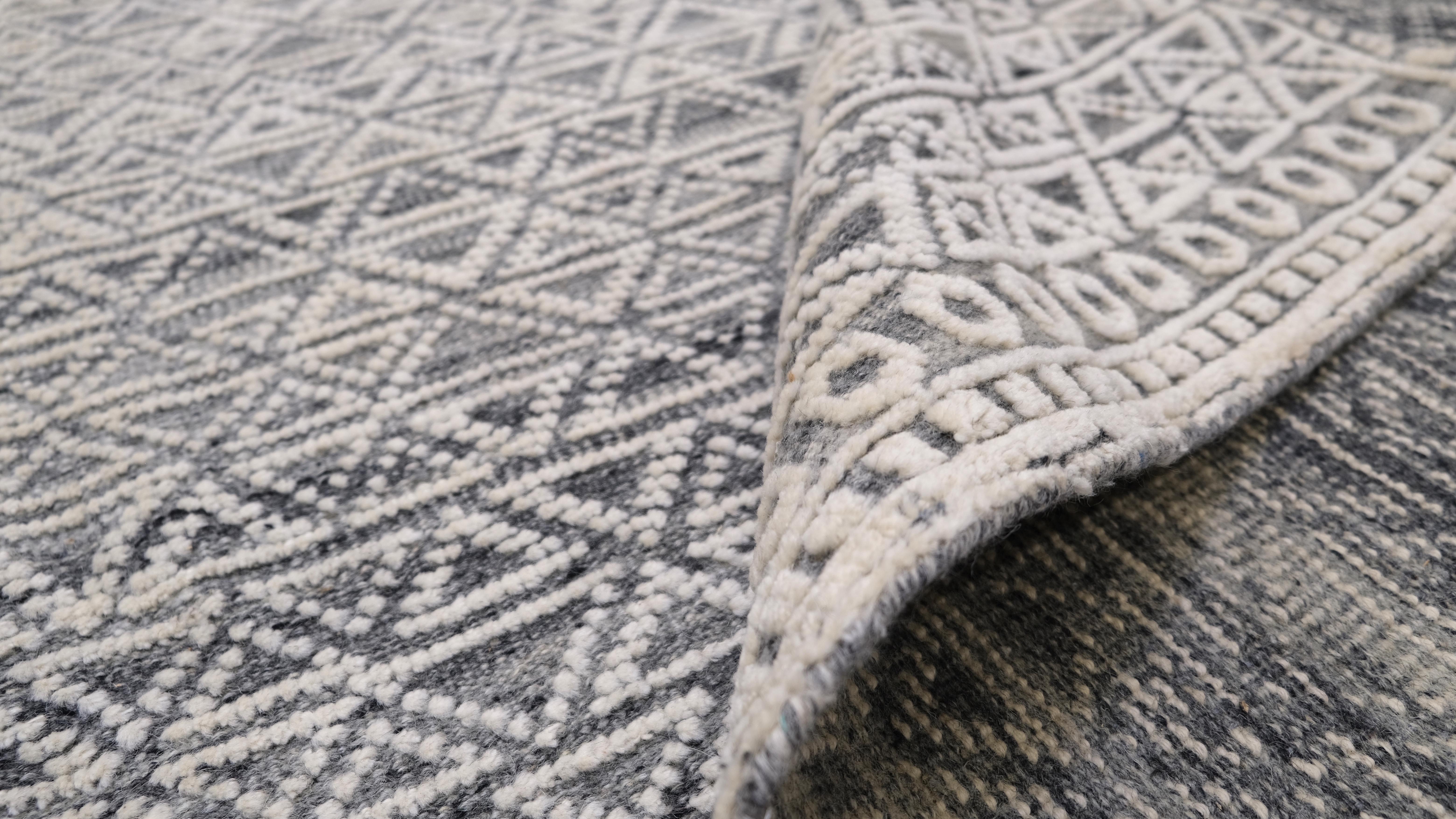 Elevate your space with this hand-knotted wool rug, featuring an intricate geometric pattern in soft gray and ivory tones. The mesmerizing design consists of repetitive triangular and lattice motifs, creating a sense of depth and texture that