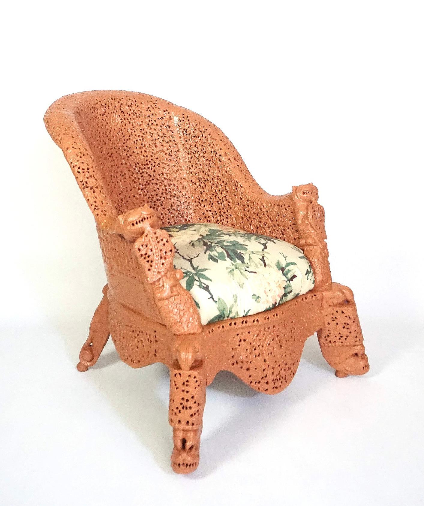 A circa 1880 Anglo-Indian, Anglo-Burmese armchair of good size having intricate pierce-carved teak frame painted deep coral, the curved crestrail dipping into 'beastie-and-boteh' canted front supports and D-shaped upholstered drop-seat; base with