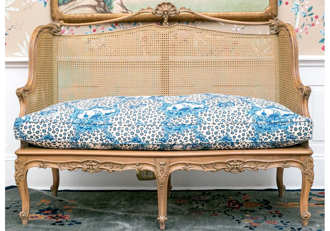 Un divano in stile Luigi XV particolarmente raffinato con una cornice intagliata in modo intricato e dettagliato, composta da maschere, viti, fiori e foglie d'acanto con una cresta a conchiglia intagliata. Il divano ha una doppia parete di canne ai