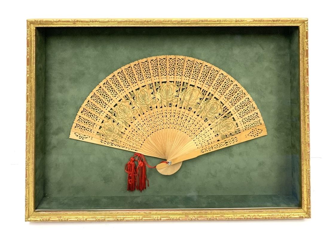 A highly decorative Carved and Tassled Sandalwood Fan mounted on a Green Velvet background and fitted in a Gilt edged custom display frame. The Fan with intricately pierced decoration and having drawn Roses along the central panel. With labels on