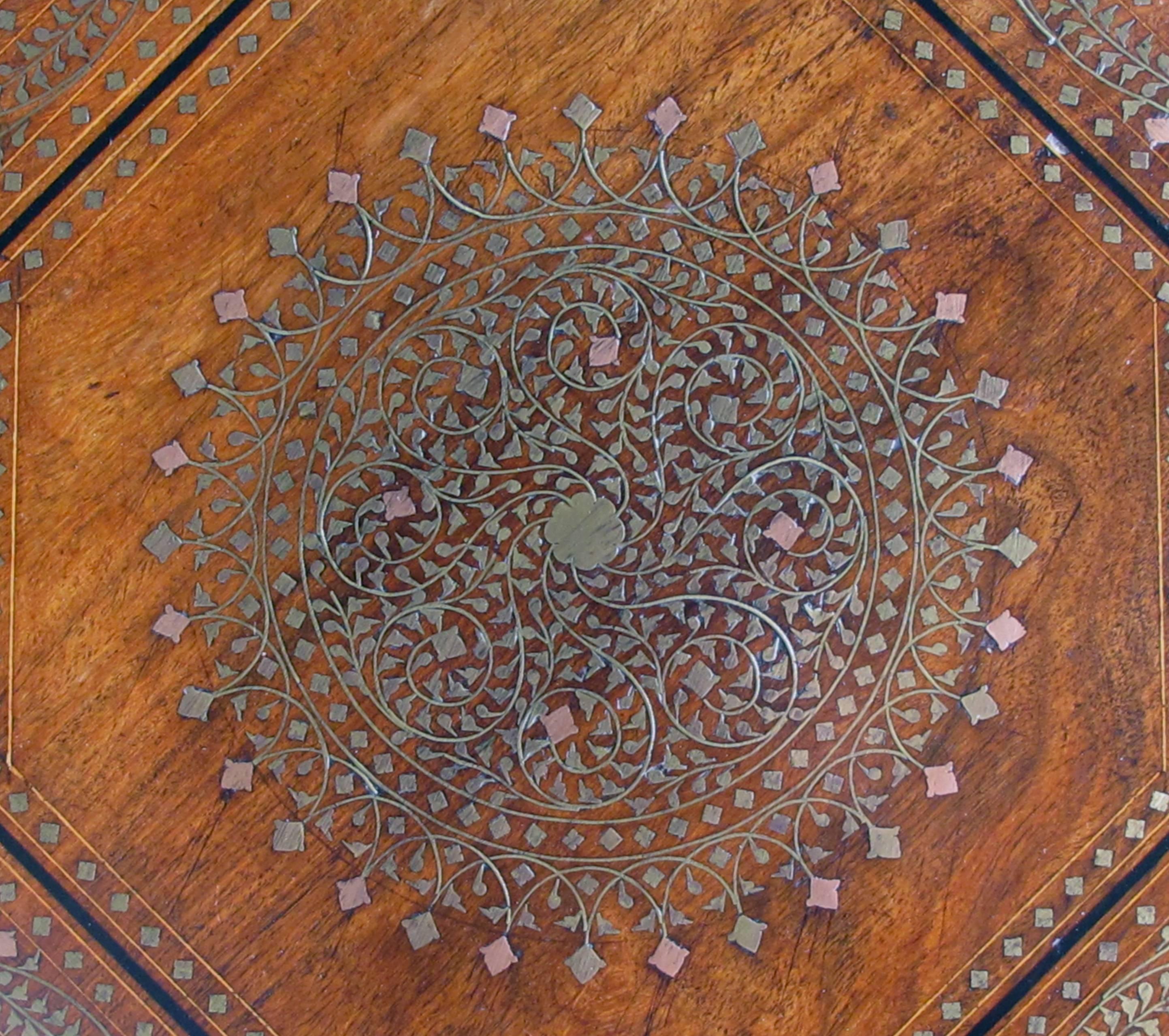 A very versatile and useful side table with octagonal top centering an interlacing copper and brass inlaid medallion surrounded by a meandering foliate branch; all raised on an arabesque base with additional brass adornment; the top affixed to the