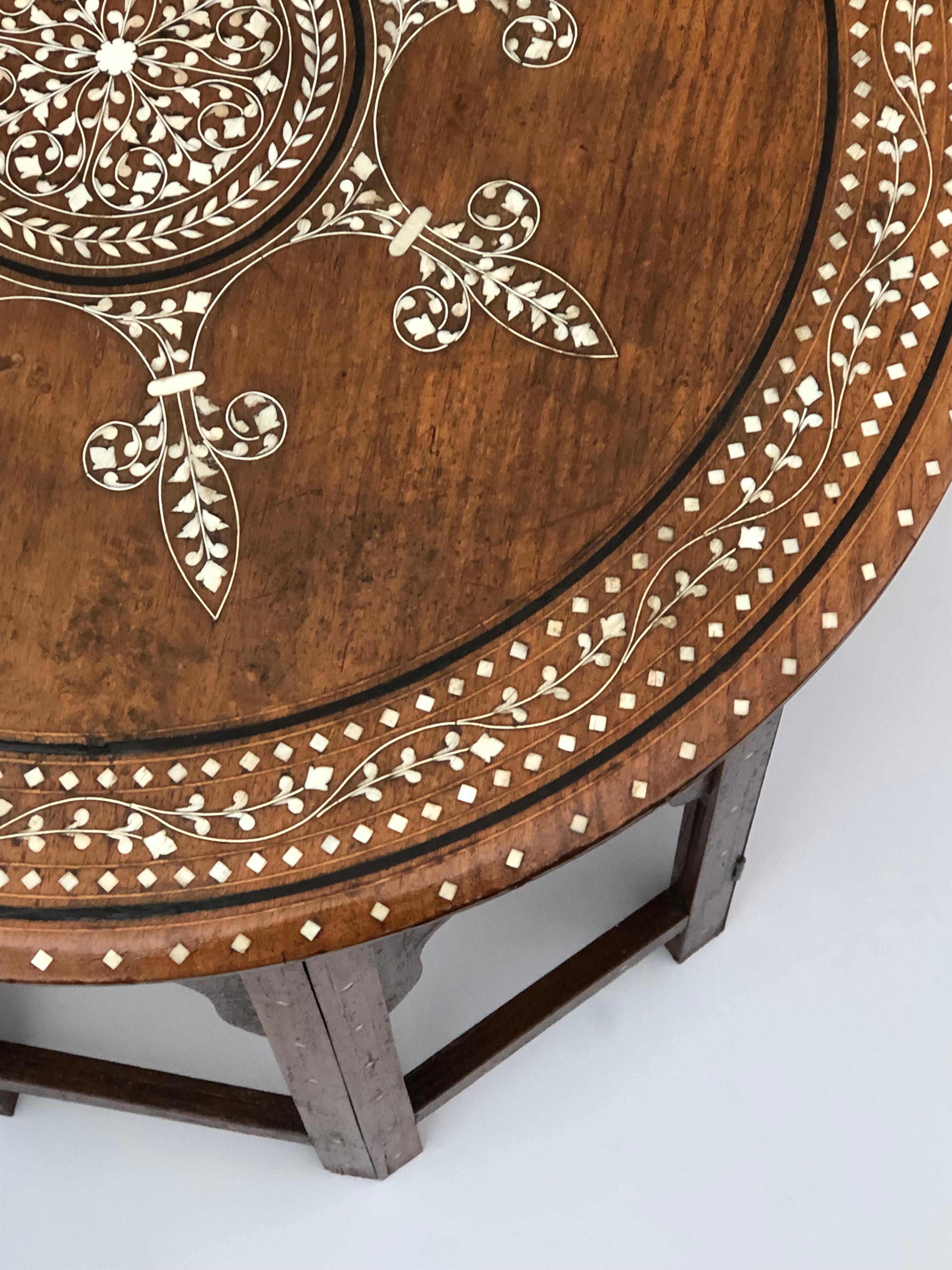 The round top centering a large inlaid medallion surrounded by a meandering inlaid foliate band; all raised on an octagonal hinged base with arabesque openings.
