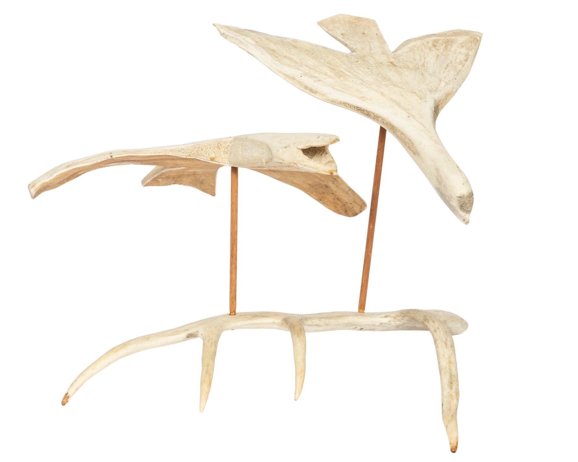 A hand carved and crafted whale bone sculpture of two birds in flight. The base is antler and the birds are suspended by simple wood supports. It is easily disassembled for convenient shipping.
