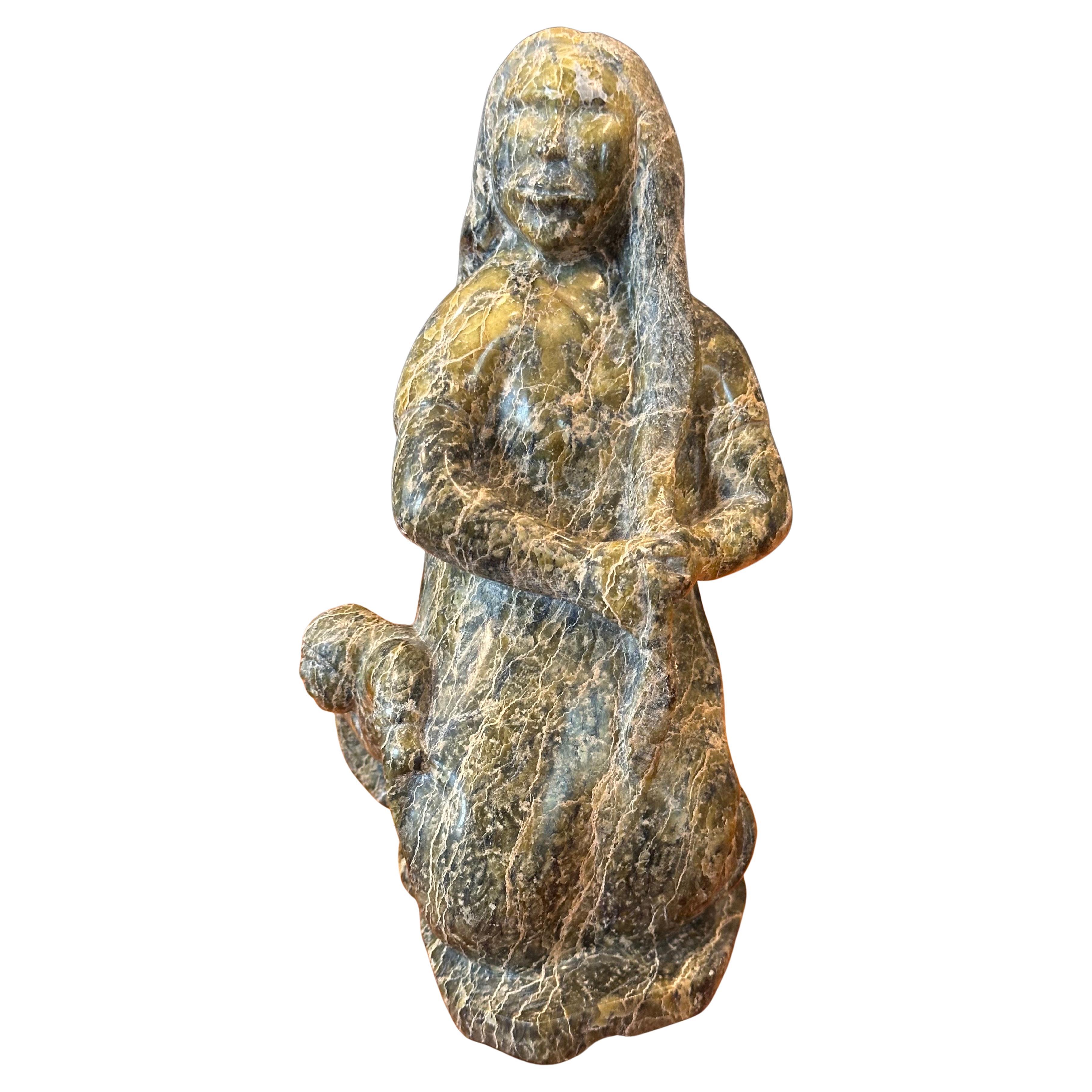 Impresionante escultura inuit de mujer y niño tallada a mano en piedra por el renombrado artista Oviloo Tunnillie, hacia la década de 1990. La pieza está en muy buen estado, sin astillas ni grietas, y mide 4,5