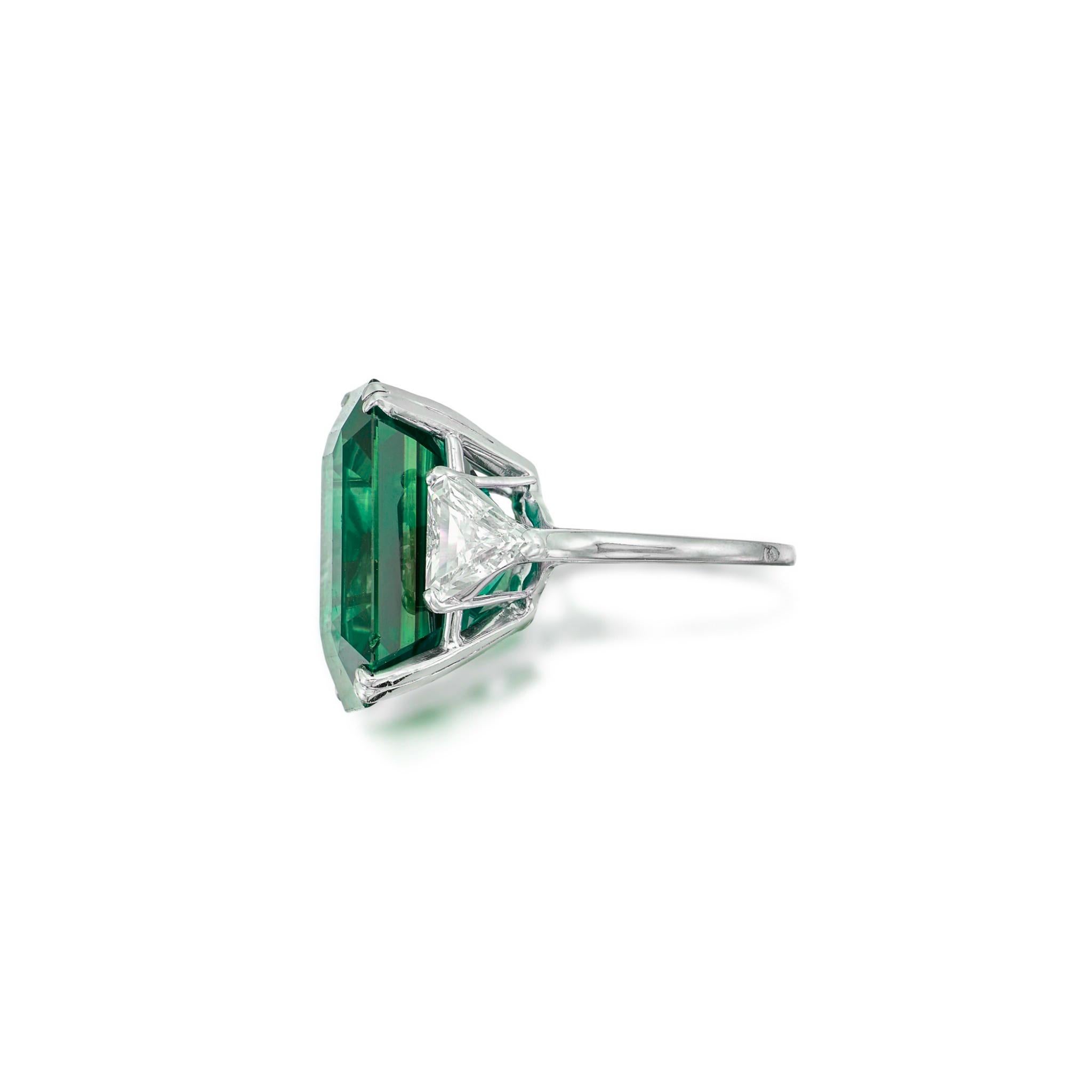 a breathtaking masterpiece: a 15-carat natural emerald, certified as minor oil, radiating with unparalleled beauty. This exquisite gemstone is elegantly set in a solid platinum ring, flanked by two stunning trillion-cut diamonds, each certified by