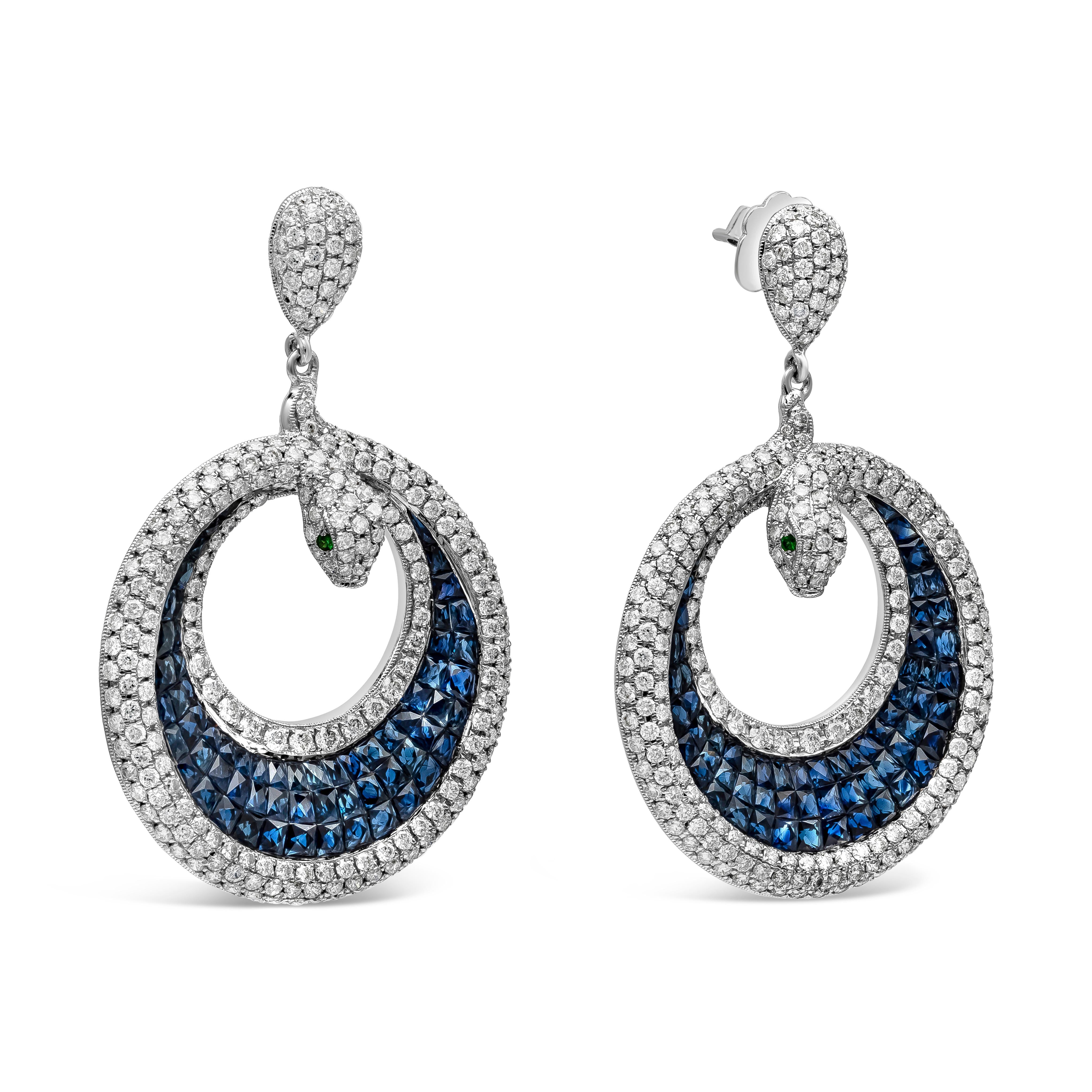 A beautiful and intricately-designed pair of dangle earrings showcasing a cluster of perfectly-matched blue sapphires accented by round brilliant diamonds, set in a beautiful serpent or snake design. The eyes of the snake are round tsavorite garnet