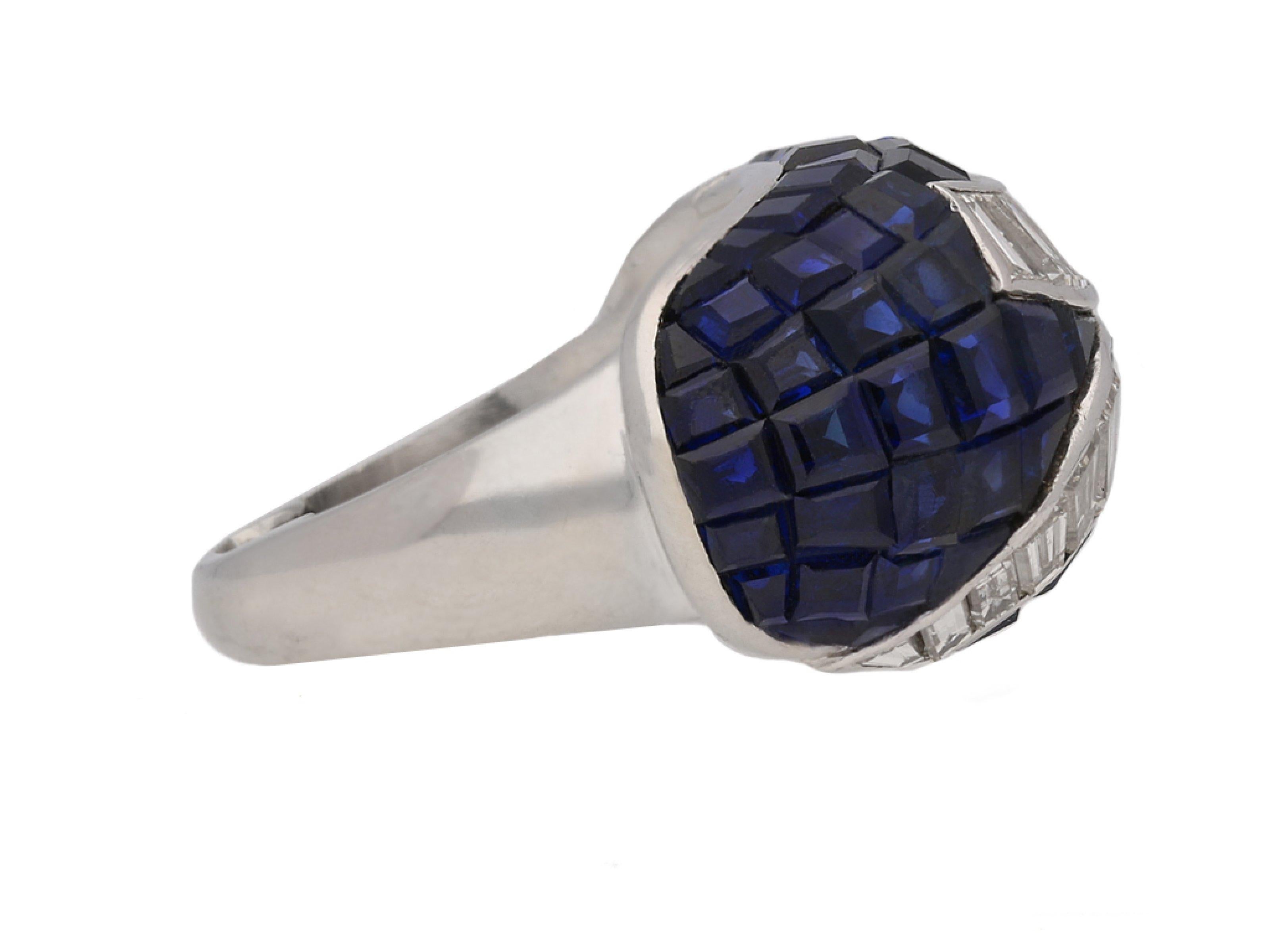 Invisible set sapphire and diamond ring. Set with seventy six tapered baguette cut natural unenhanced sapphires in open back invisible settings with an approximate total weight of 12.50 carats, also embellished with two opposing scrolled elements