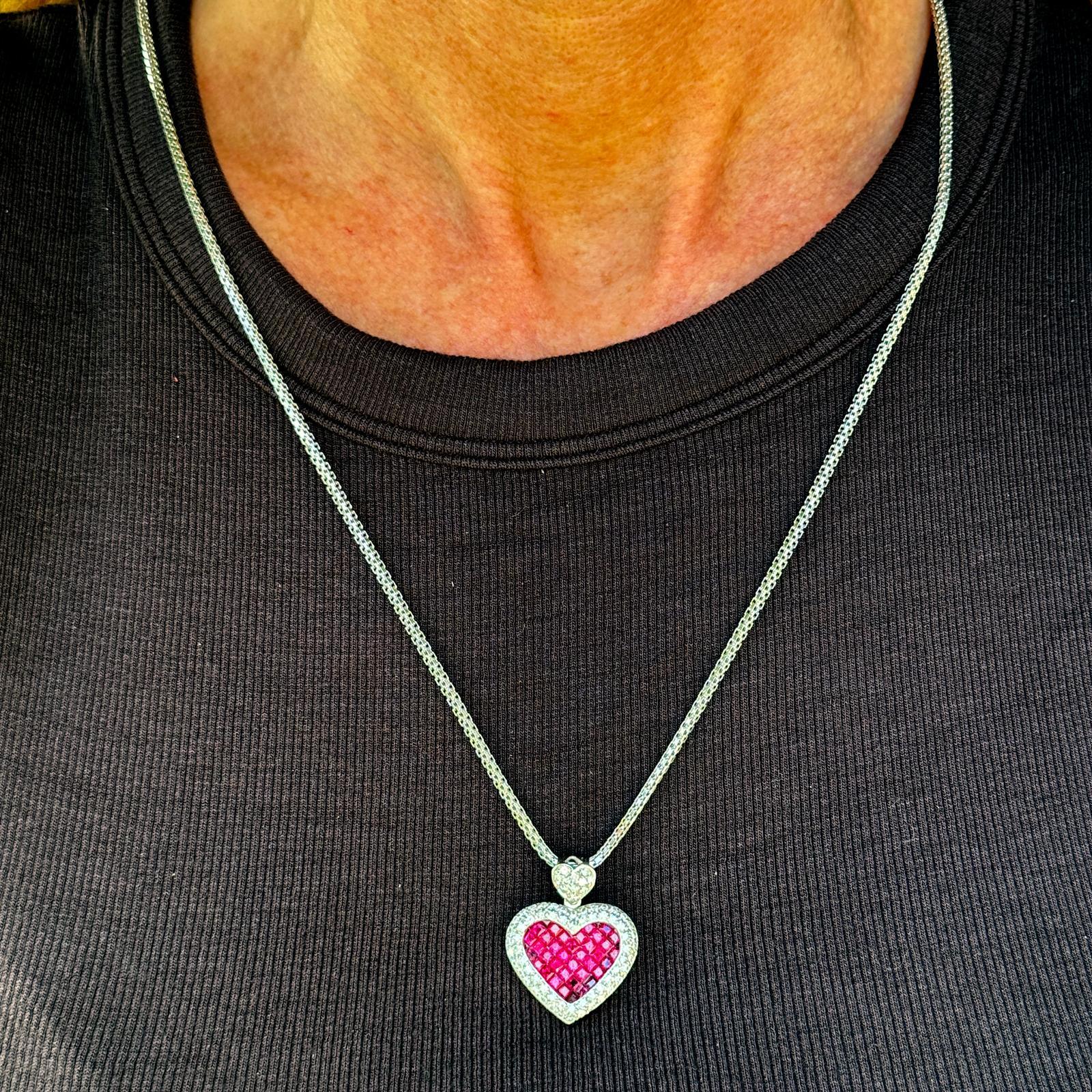 This elegant necklace pairs a 23.5-inch 14K white gold box chain with a striking 18K white gold heart pendant measuring 1.00 x .80 inch. The pendant is adorned with square rubies invisibly set, creating a smooth, seamless surface that showcases the