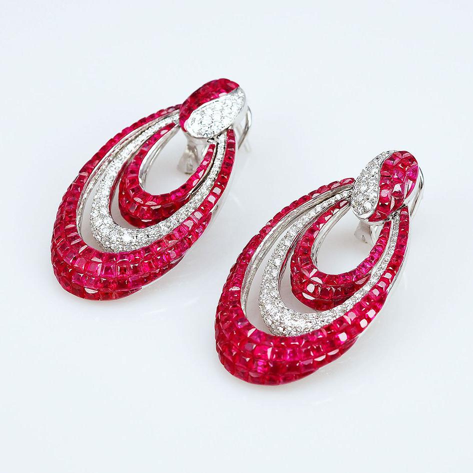 Invisibly-set ruby and diamond drop earrings, featuring three graduating crescent-shaped oval drops in rubies and diamonds. Handcrafted in polished 18k white gold. Rubies weighing 24.78 total carats. Diamonds weighing 1.32 total carats (G-H color,
