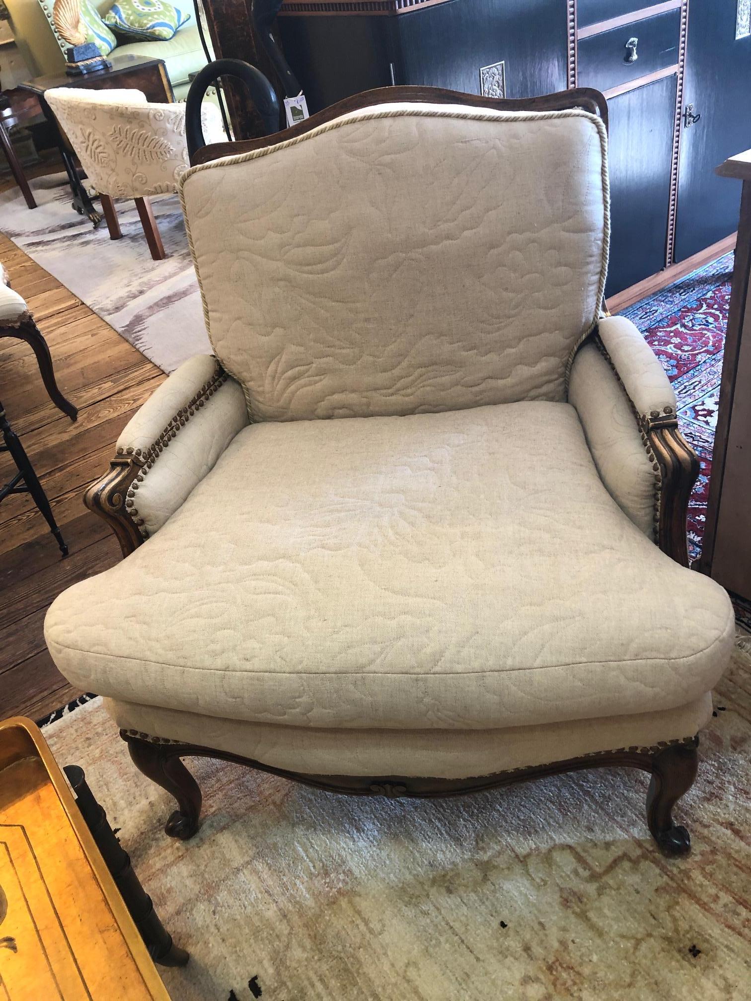 A big comfy neutral French style bergere having handsome carved walnut frame and creamy taupe quilted upholstery front, back and sides. Finished with nailheads and decorative welting.