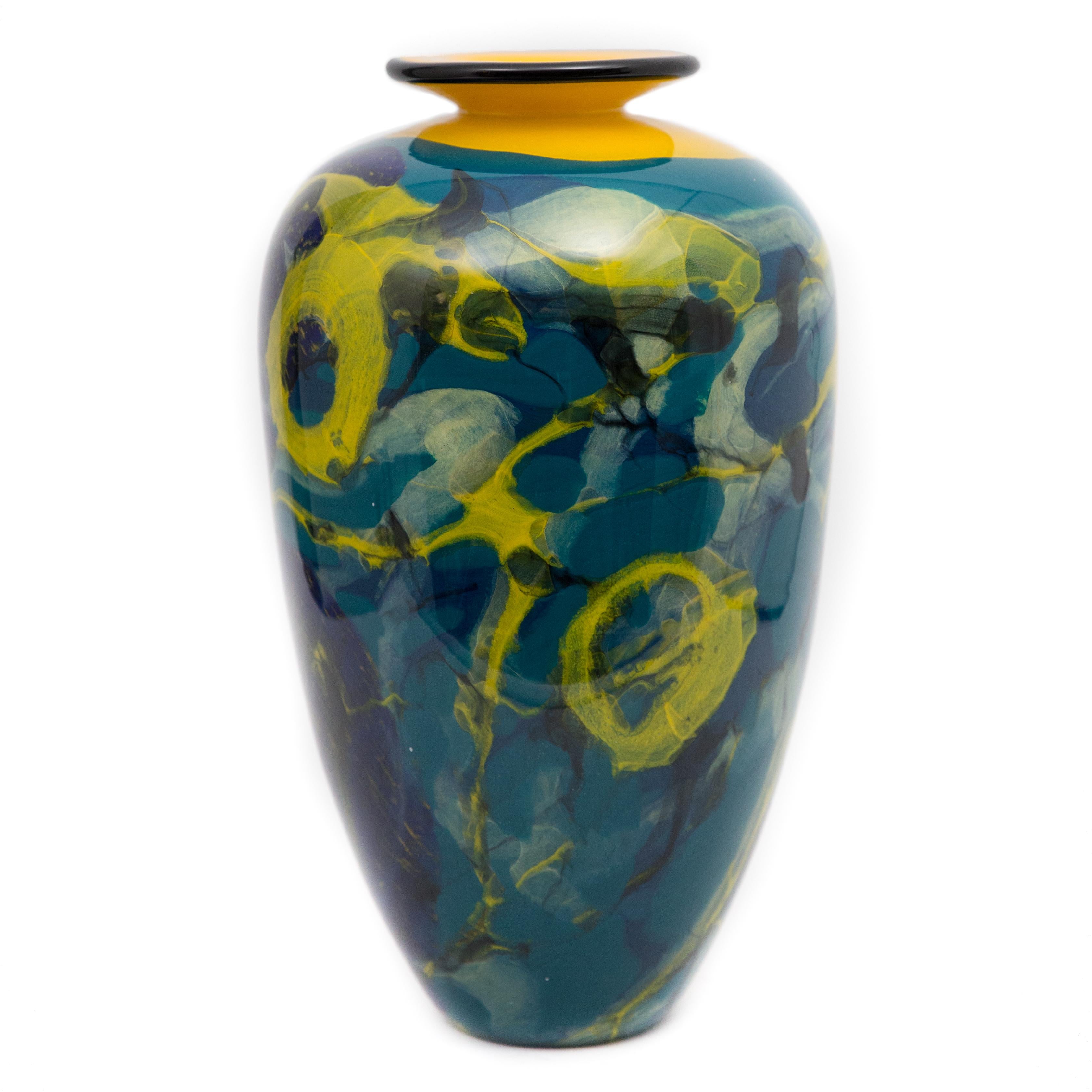 This vase is a vibrant red yellow and blue work that was created by Ioan Nemtoi. The artist signed the vase. The vase has a black rim, yellow and red throughout, on a blue ground. Born in Romania in 1964 he attended the Academy at Bucharest, his