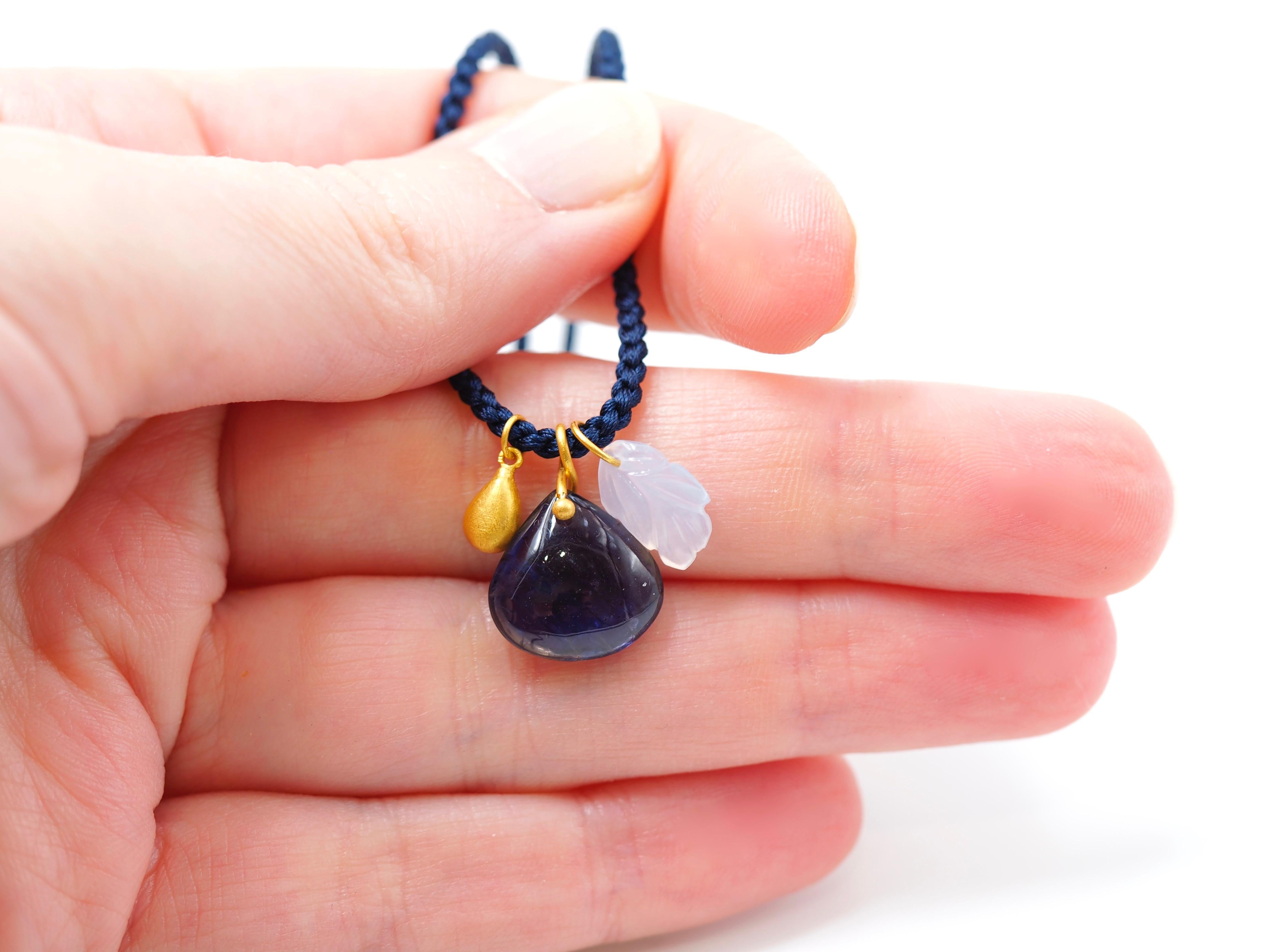 This delicate necklace is composed of 3 pendants on a long braided silk rope:
- a iolite cabochon with a twisted gold ring
- a 22kt gold drop
- a blue chalcedony leaf
All stones have been hand-cut, hand-faceted and handmade by our skilled