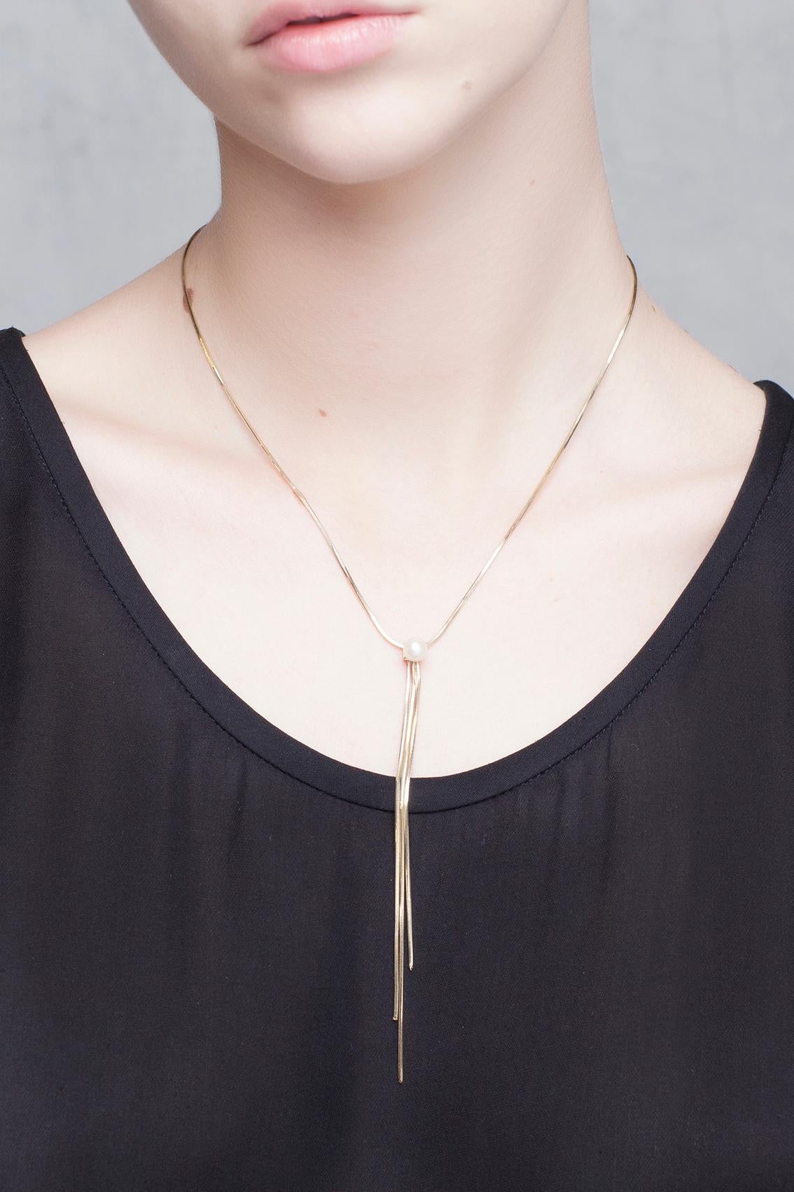 Balancing its design between minimalism and avant-garde, Iosselliani captures the essence of elegance with this 9 Karat yellow gold necklace embellished with a central tassel made of 9 Karat gold threads adorned by a central freshwater pearl. Pearls