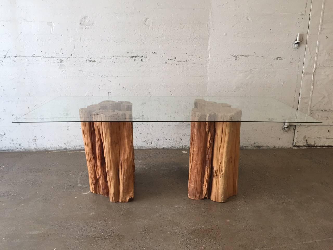 Halved Ipe wood trunk pedestal dining table with a glass top. The trunks have natural splitting and grain variations throughout.