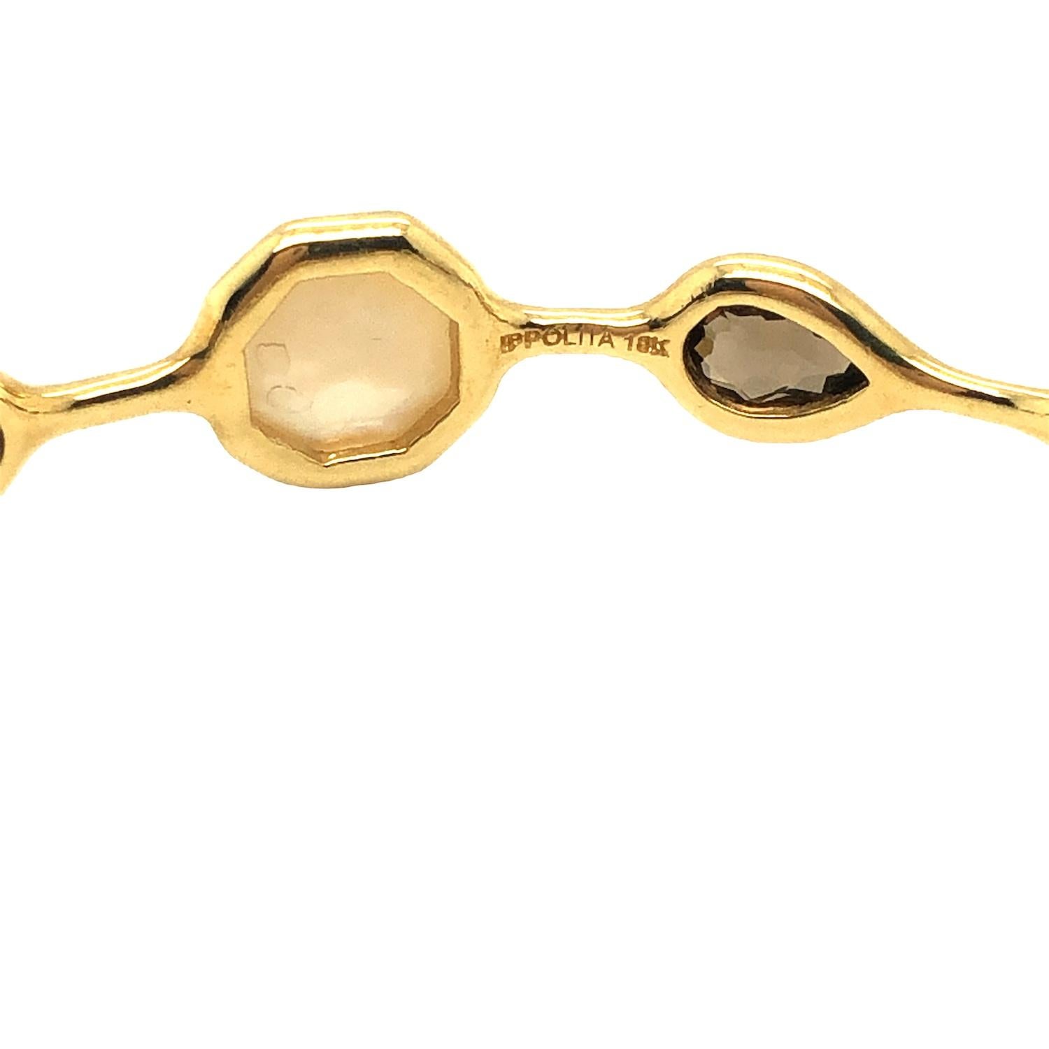 The Rock Candy Collection from Ippolita showcases a bangle bracelet adorned with an array of exquisite gemstones, including mother of pearl, smokey quartz, and onyx, all elegantly arranged in 18K yellow gold. This bracelet measures 8 inches in