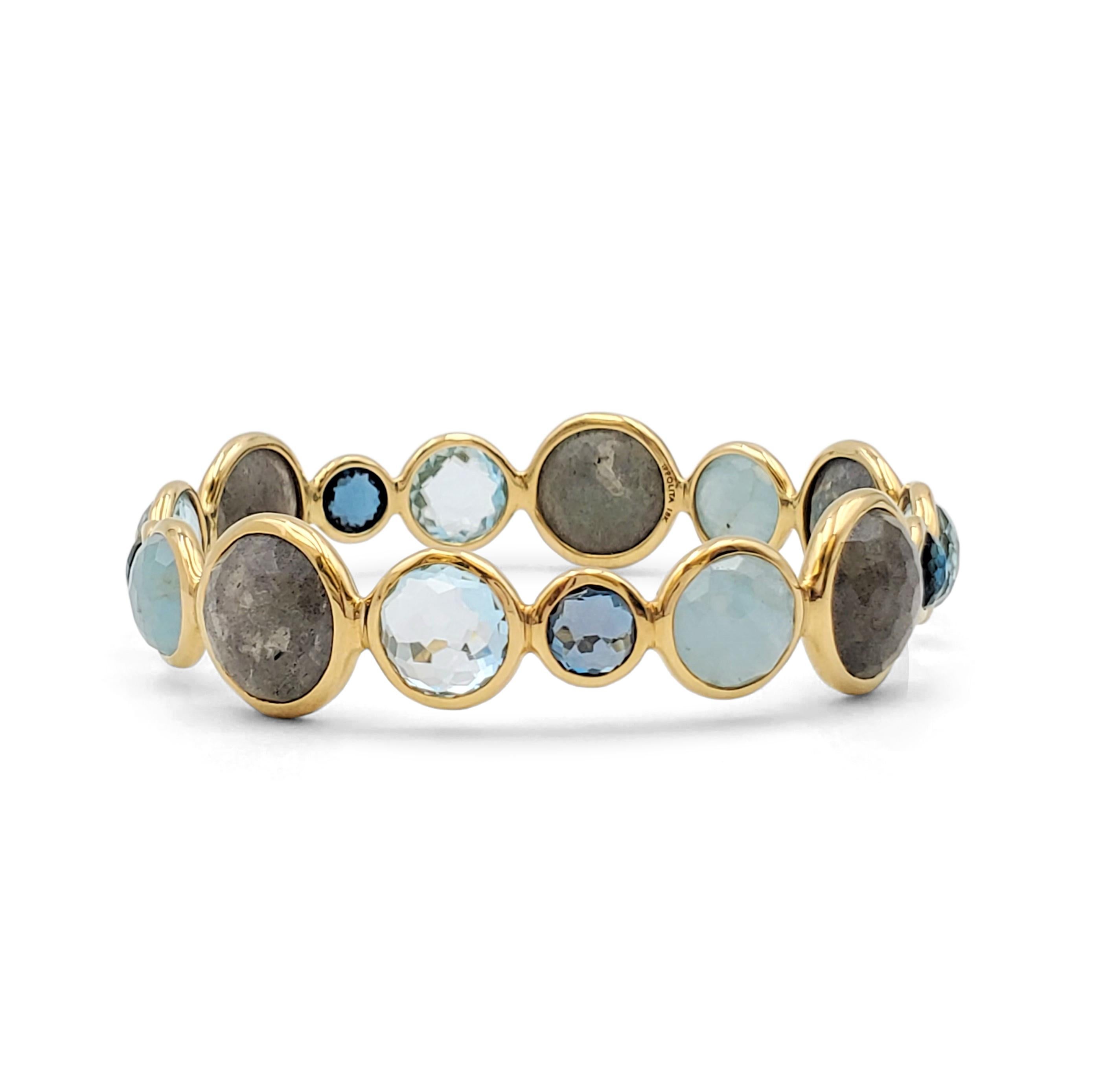 Authentic Ippolita 'Rock Candy' bangle crafted in 18 karat yellow gold set with 16 bezel-set, multi-sized, rose cut blue gemstones. Misty labradorite and watery topaz stones in multiple shades are alternated throughout. The bangle is stamped 18K and
