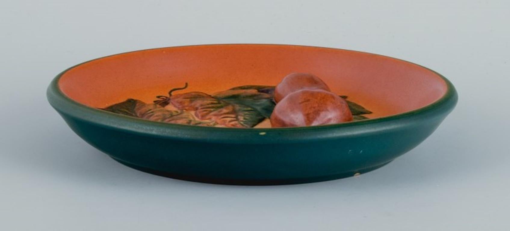 Ipsen's, Denmark. 
Ceramic bowl with leaves and pumpkins, glaze in shades of orange-green.
Model 8.
1920s-1930s.
In excellent condition.
Marked
Dimensions: D 17.0 x H 3.0 cm.