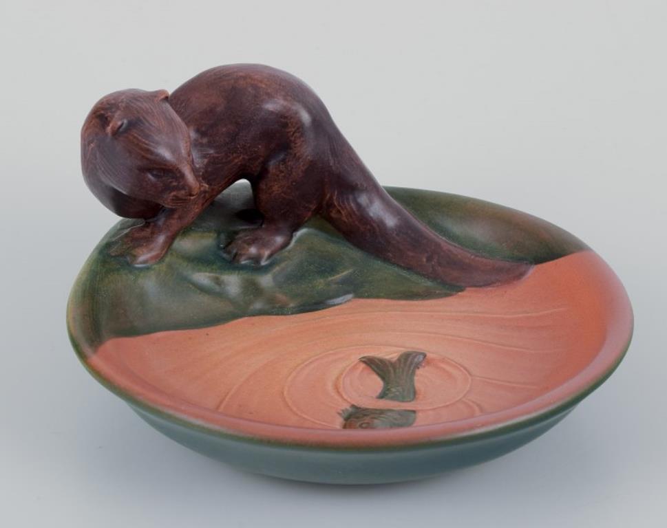 Dinamarca de Ipsen.
Cuenco de cerámica con una nutria y un pez en el agua.
Modelo raro. 
Model No: 219
Fechas: 1930s.
Marcado.
En perfecto estado.
Dimensiones: P 14,5 cm. x A 7,5 cm.