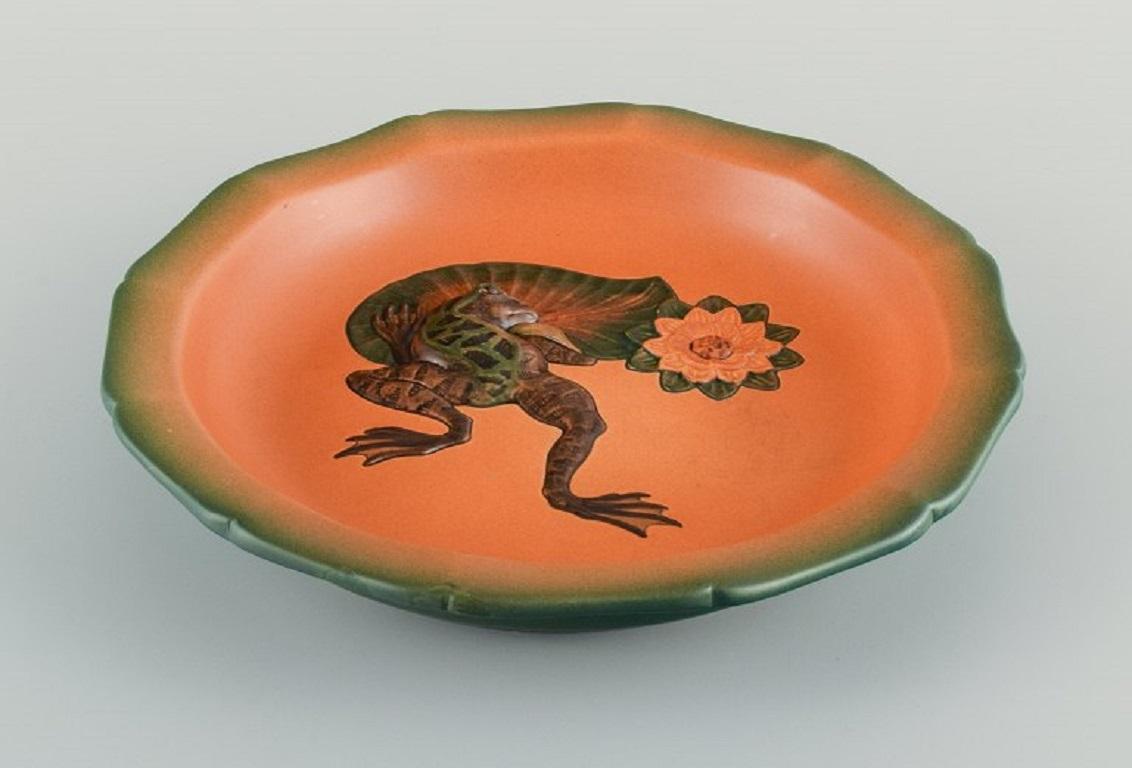 Ipsens, Denmark. 
Circular dish in hand-painted glazed ceramic, with a frog on a water lily leaf.
Model number 122.
Approx. 1920.
In excellent condition.
Marked.
Measurements: D 27.0 x H 5.0 cm.