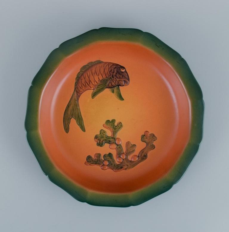 Ipsens, Denmark, dish with fish with glaze in orange-green shades.
Model number 139.
1920s.
In excellent condition.
Dimensions: D 27.5 x H 4.0 cm.

