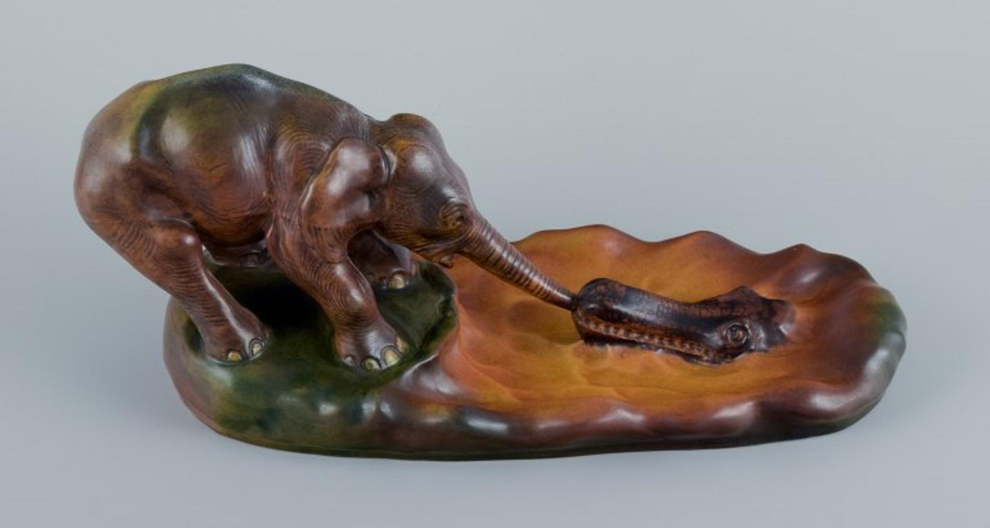 Ipsens, Denmark, Elephant and Crocodile. Ceramic figurine group, glaze in orange-green shades.
From Rudyard Kipling's tale of how the baby elephant got its long trunk by the “Great Grey-Green-Greasy Limpopo River”
Model number 274.
1920s.
In