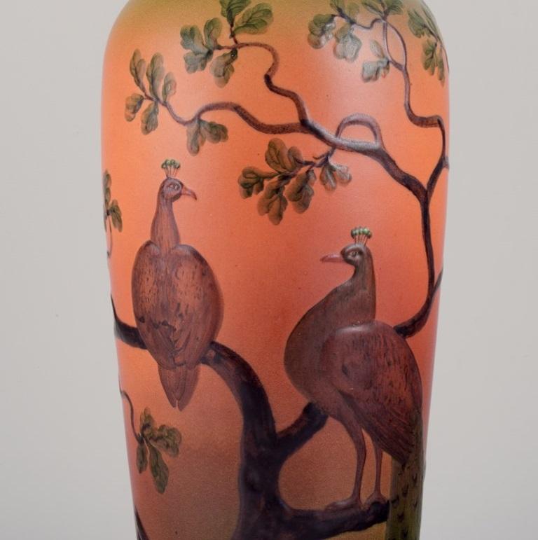 Ipsens, Denmark. Large table lamp in ceramic.
Motif of peacocks sitting in a tree.
Orange and green tones.
Model number 76.
Approximately 1920.
Marked.
In excellent condition.
Bakelite socket.
Dimensions: Height 46.0 cm x Diameter 14.0 cm.