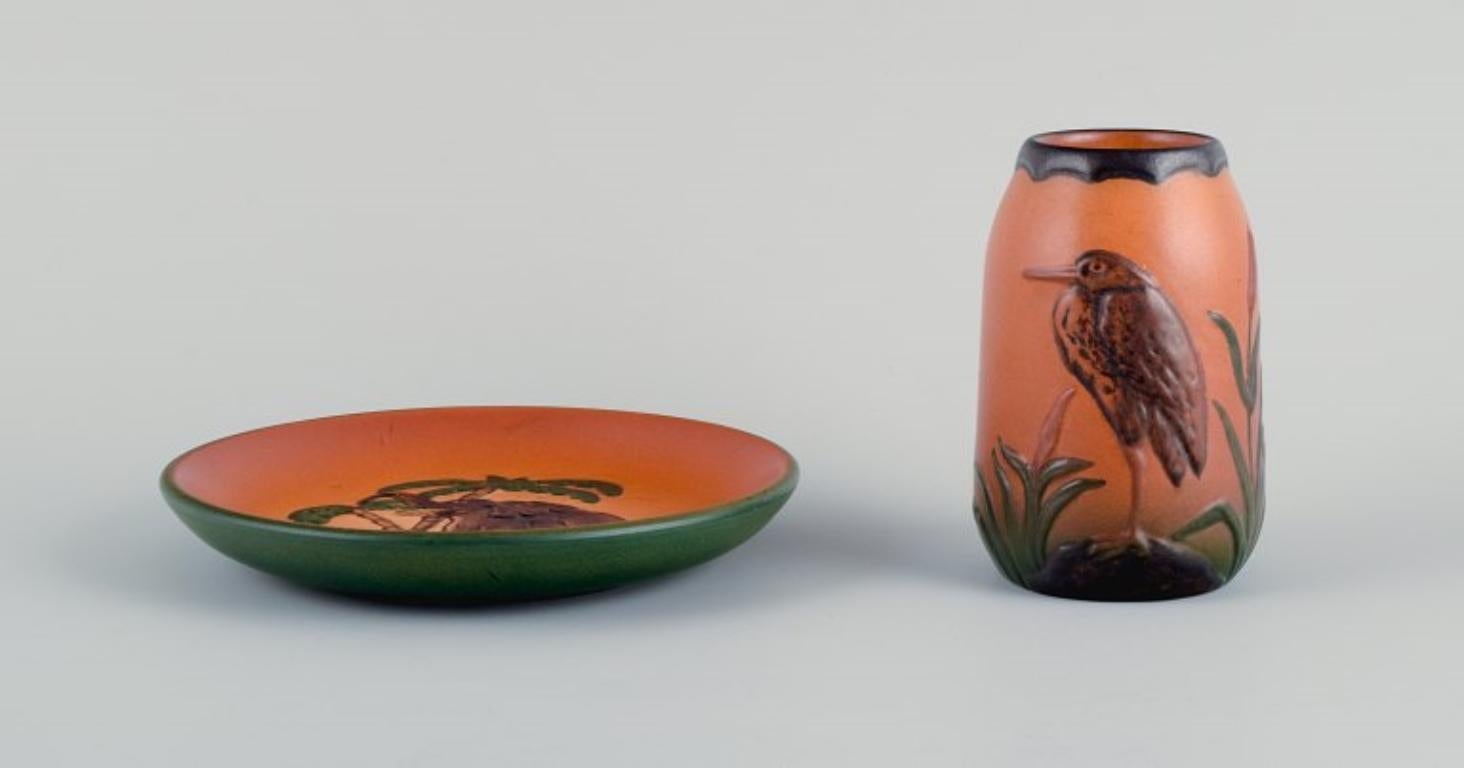 Ipsens Enke, a ceramic vase and a ceramic dish.
Malibu and elephant motif.
Glaze in orange-green shades.
Approx. 1920/30s.
In perfect condition.
Marked.
Model numbers. 749 and 7.
Vase: H 11.5 x D 7.0 cm.
Dish: D 16.3 x H 3.0 cm.
