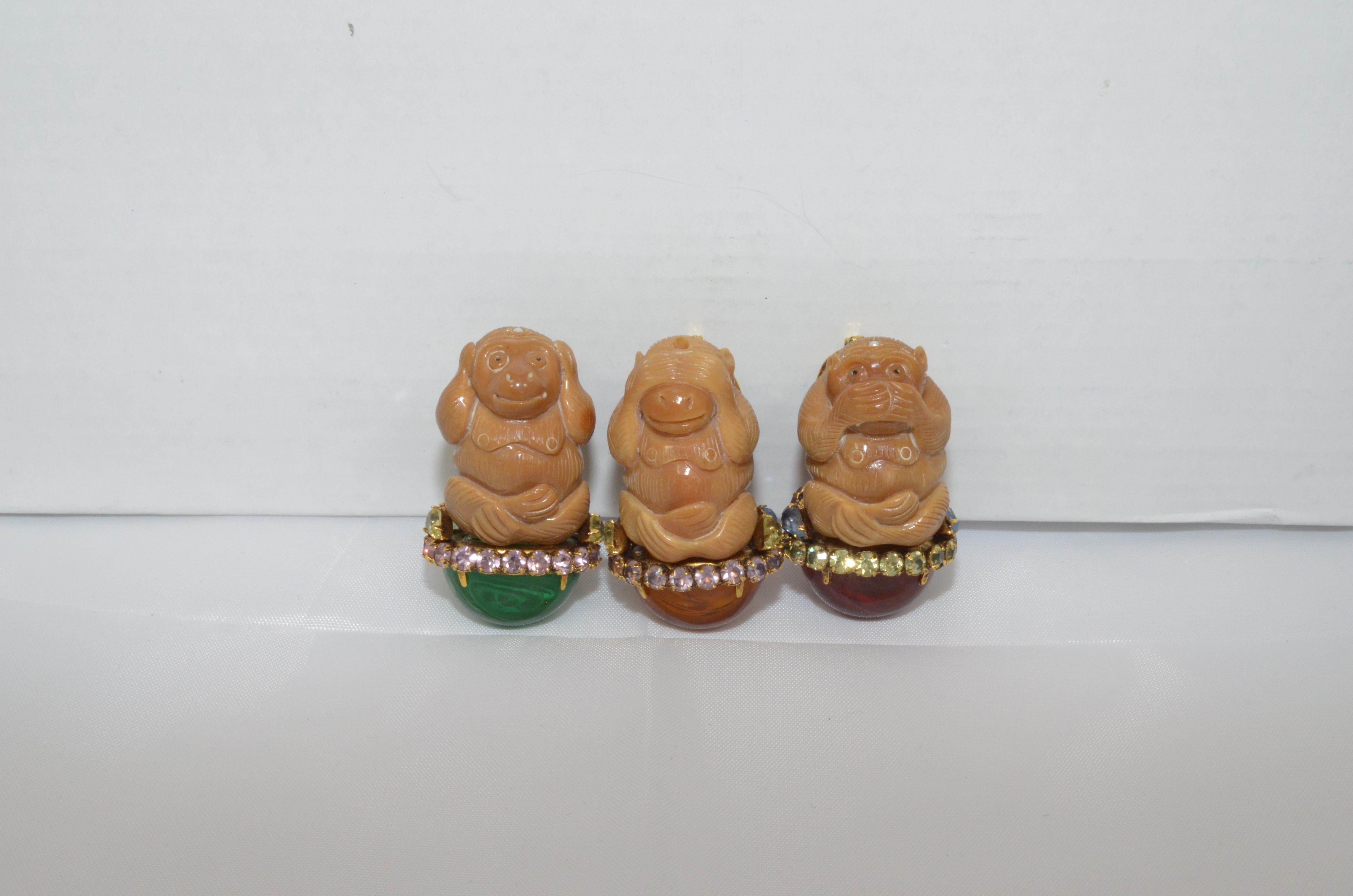 A trio of Iradj Moini Hear-No-Evil, See-No-Evil, Speak-No-Evil monkey brooches. Each brooch features a plastic sitting monkey in one of the three fabled positions with covered eyes, ears or mouth. The monkeys are sitting on top of glass stones.