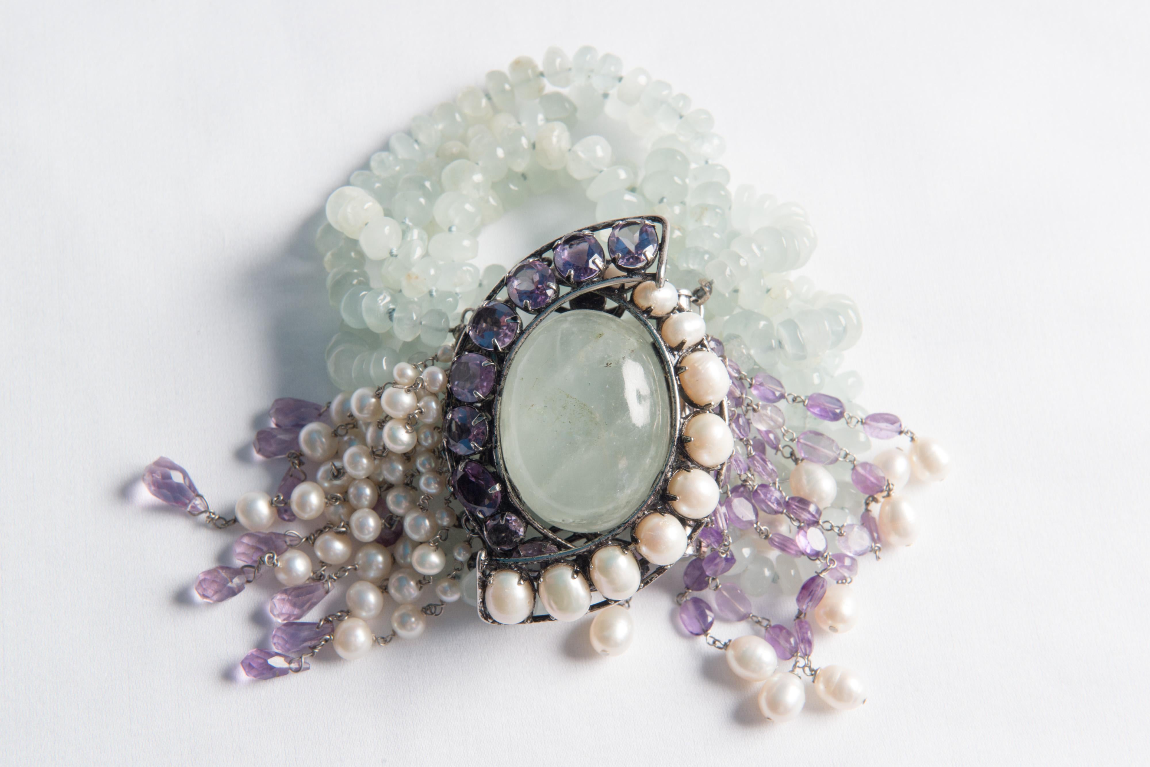 Large Iradj Moini eight strand pale green beaded bracelet with huge oval pale green cabochon gemstone surrounded by amethyst gems and pearls and multiple strands of dangling pearl and amethyst stones.
Removable brooch.