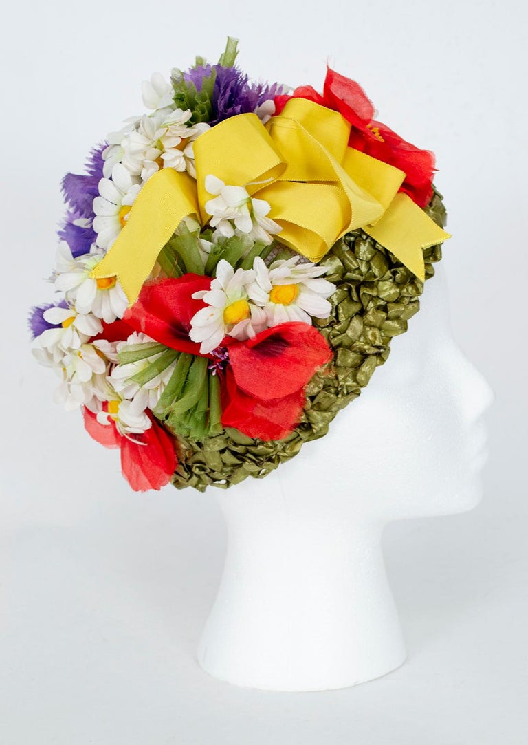 A hat worthy of Jean Shrimpton’s 1962 Vogue cover, this floral turban is a celebration of spring that can’t help but make you smile. A profusion of daisies, carnations and poppies carpets “grass” woven of green raffia, all topped with a yellow