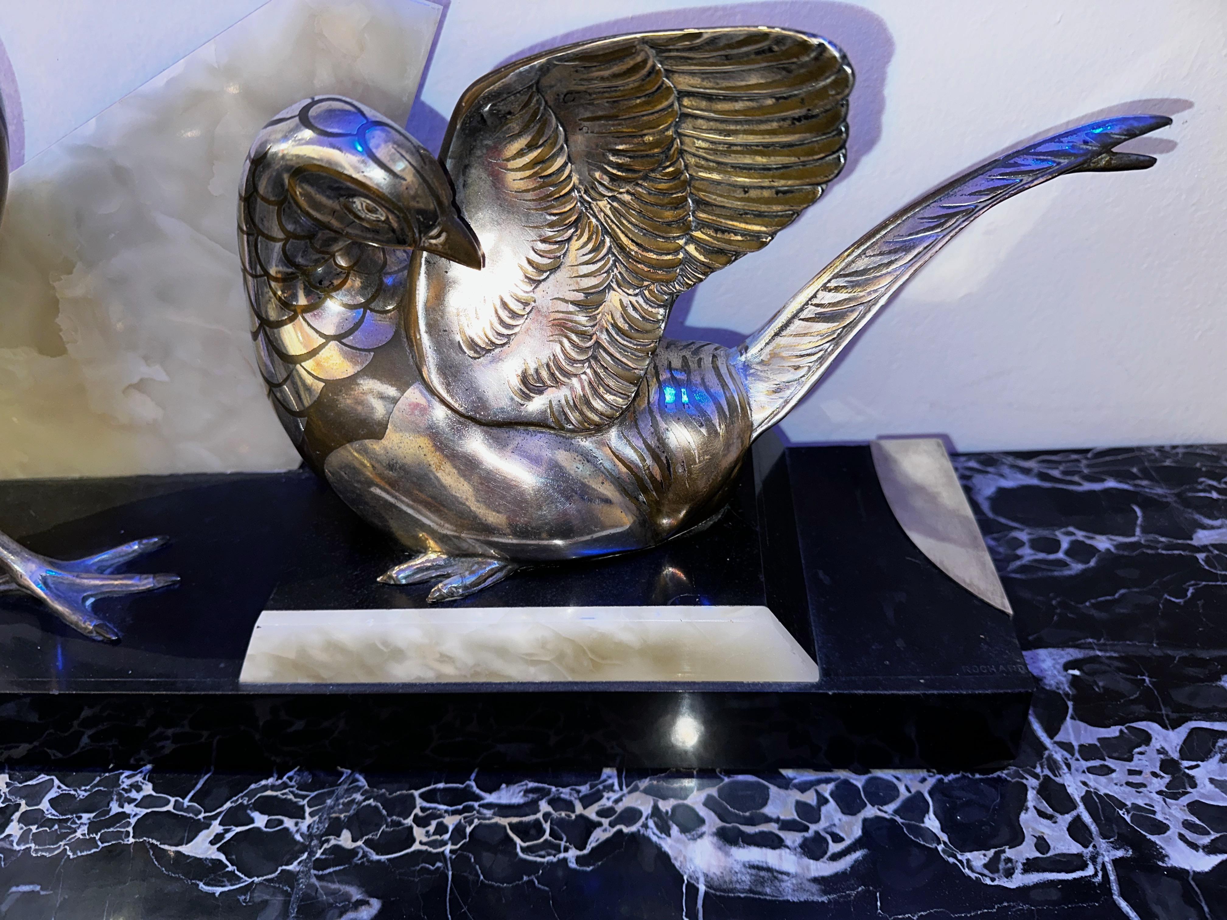 The Art Deco Birds Statue by Rochard is a unique treatment of two pheasant birds in contrasting positions. Both figures are mounted on a beautiful base crafted in three colors: marble, quartz, and silver metal. The signature Rochard is etched in the