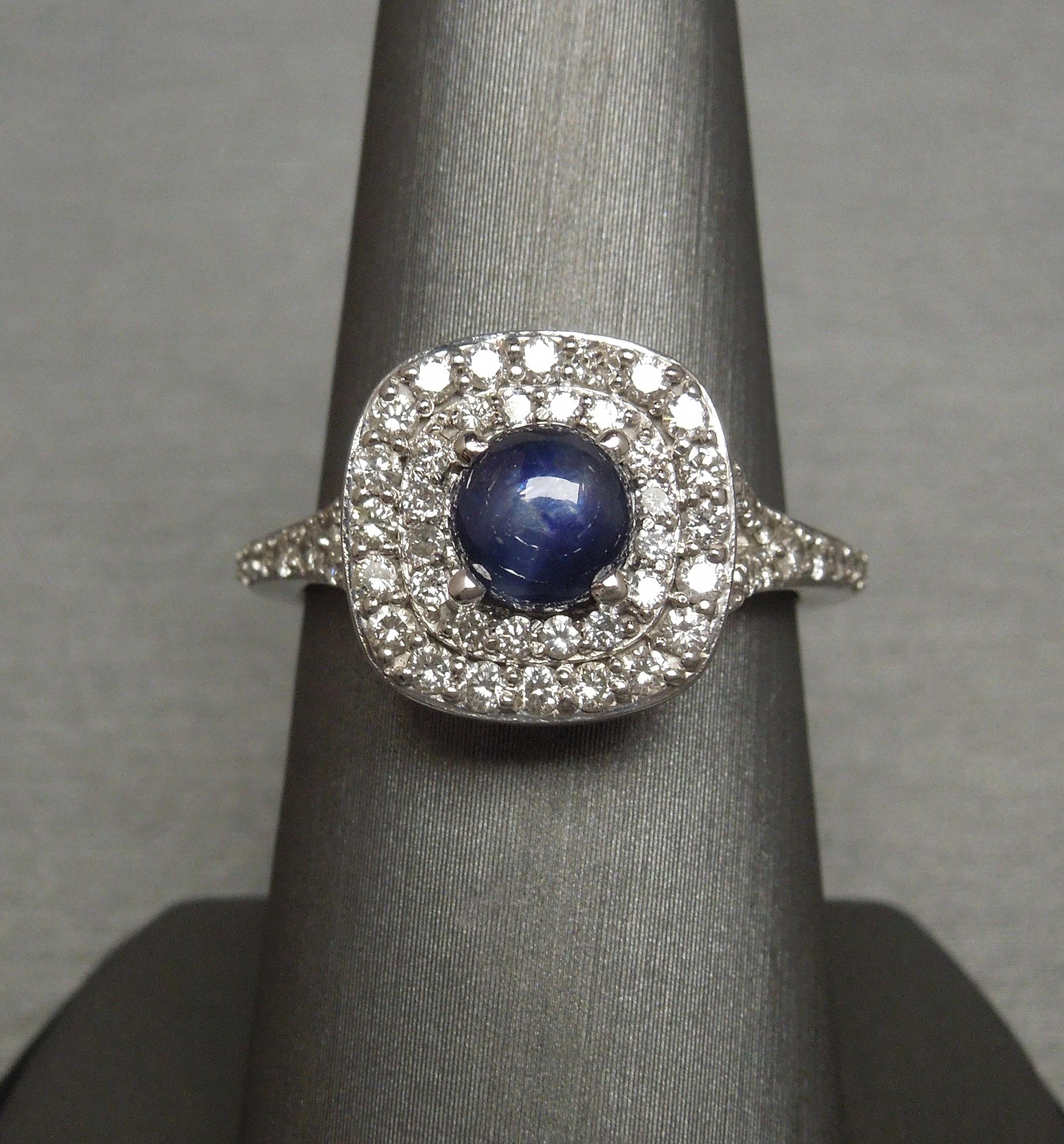 This Sapphire & Diamond Halo Ring features a central Round Cabochon cut 1.58 carat Iridescent Blue Sapphire at 5.9mm in diameter, secured in a 4-prong setting - with slight indications of striation [natural inclusions coming up to surface of stone,