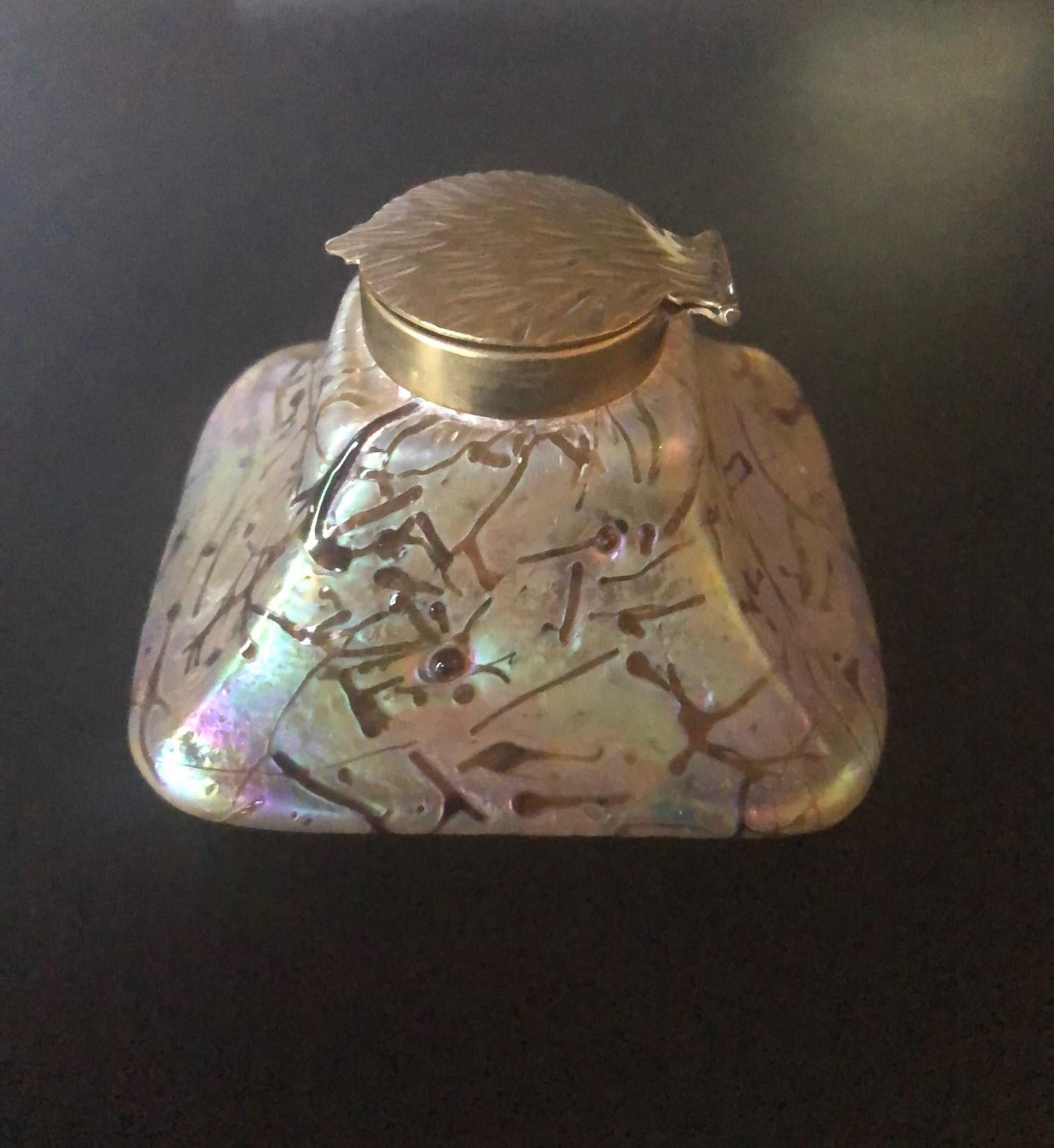 Stunning early Art Nouveau threaded iridescent art glass inkwell, circa 1900s. The piece features a gorgeous array of rainbow iridescence from pinks to blues to greens to browns. The inkwell is capped with a gorgeous brass leaf motif lid and rim.