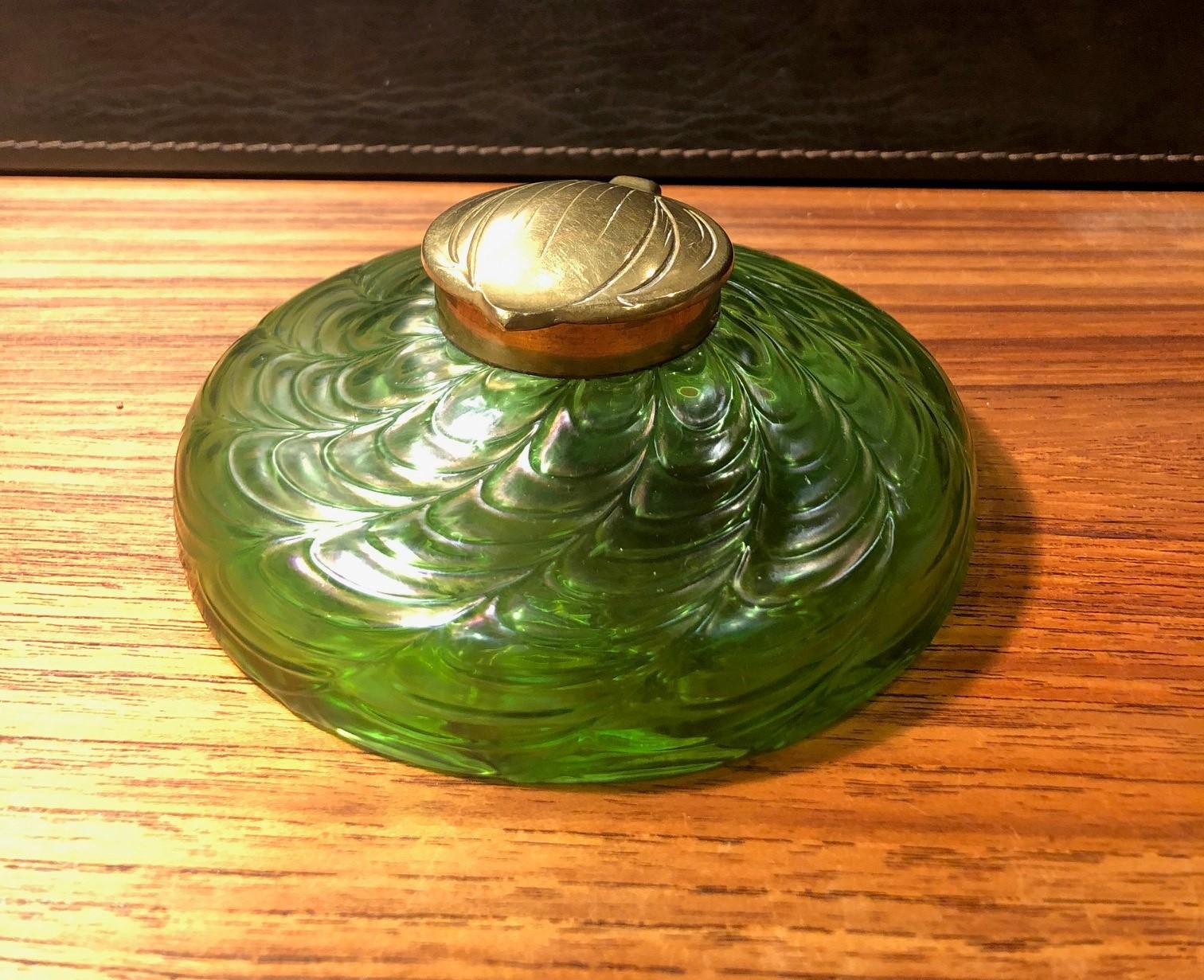 Stunning early Art Nouveau iridescent art glass inkwell, circa 1900s. The piece features a gorgeous array of rainbow iridescence from greens to blues to yellows. The inkwell is capped with a gorgeous brass leaf motif lid and rim. Also includes