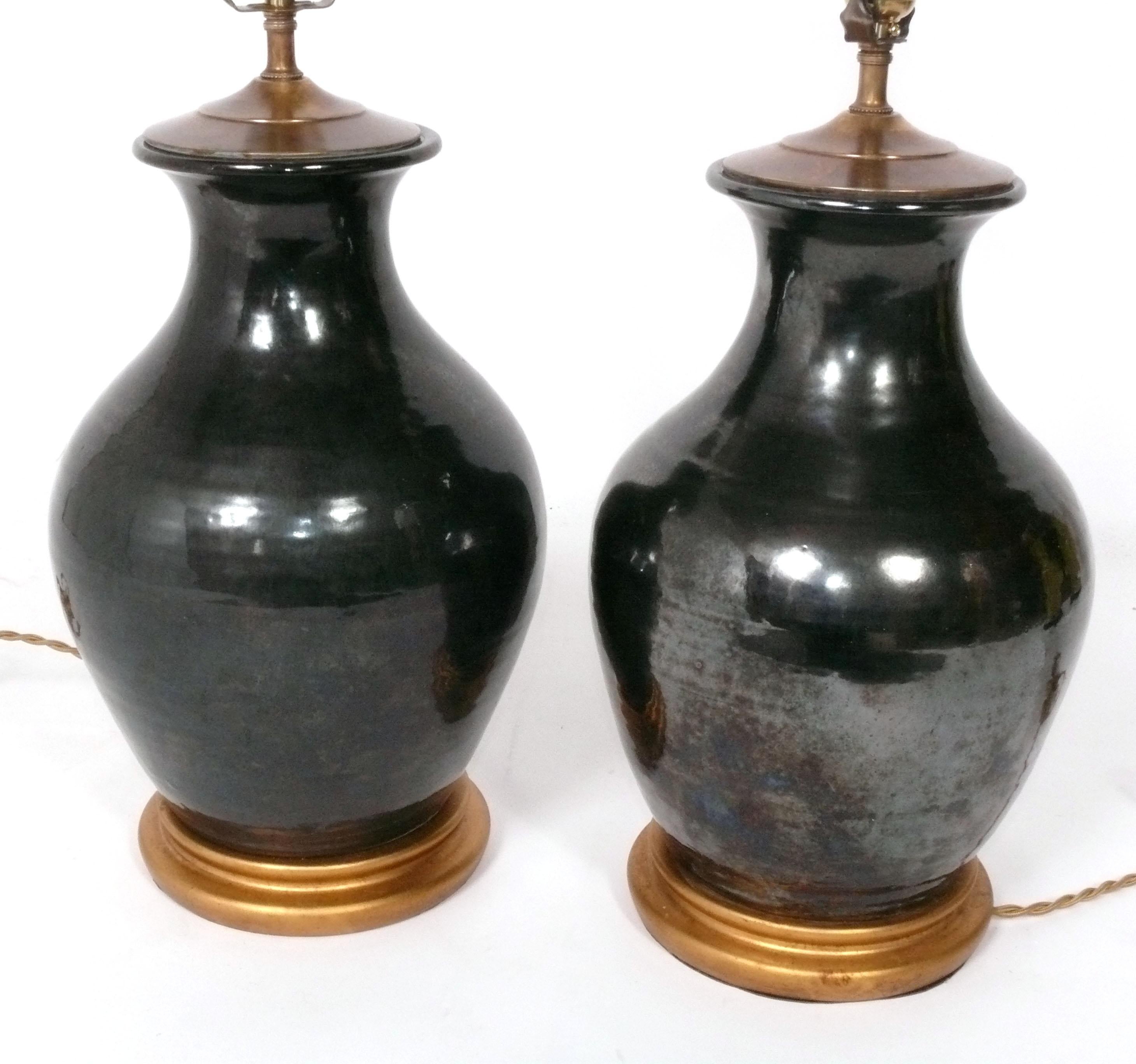 Pair of Iridescent Black Ceramic Lamps with Gilt Wood Bases, in the manner of Christopher Spitzmiller, American, circa 1990s. They have been recently rewired with gold braided cloth cords. The height to the top of the sockets is 21