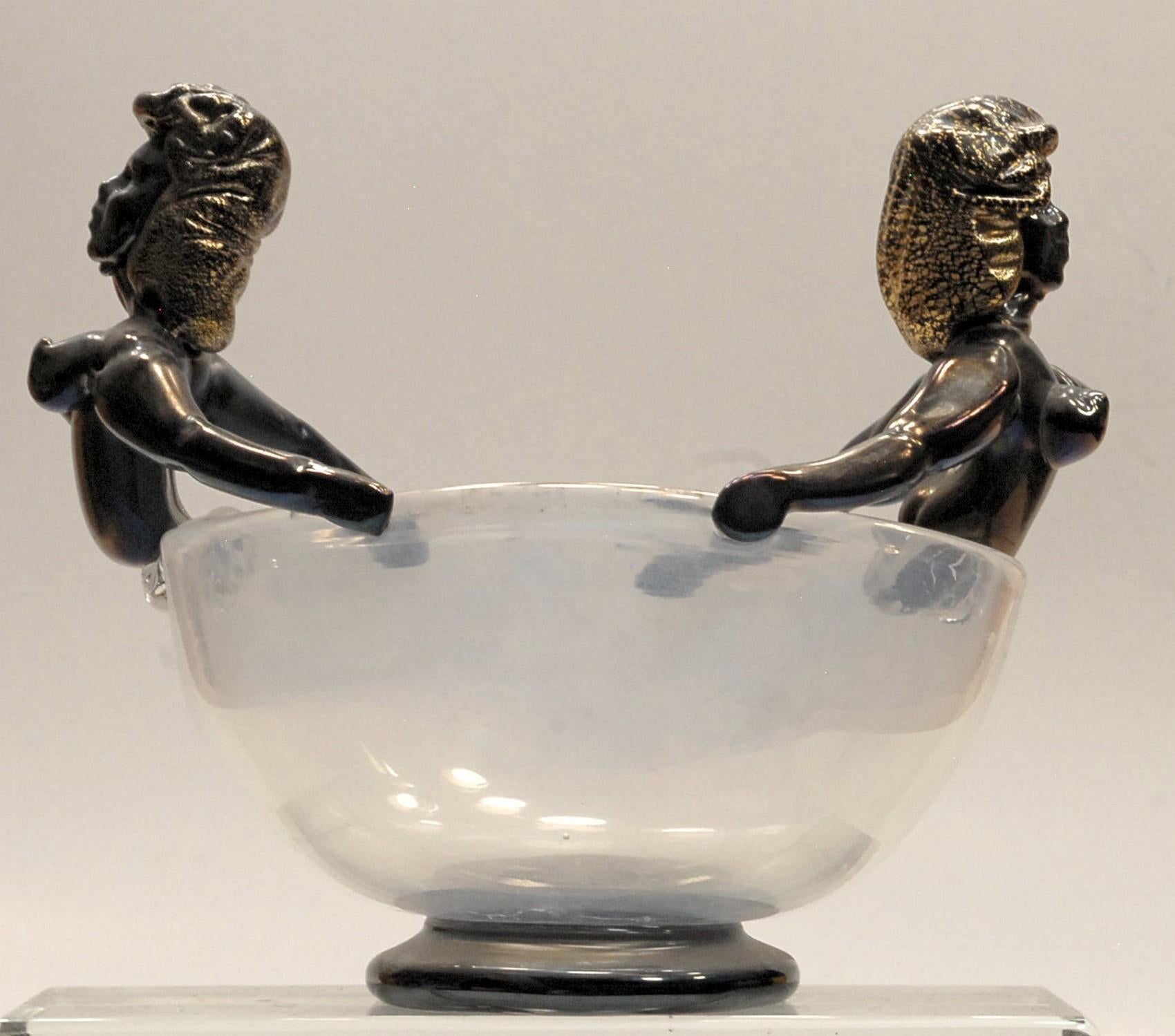 This shows the Classic Murano figurine head with the casque hair position. The bowl has been waved to hot attach the two busts that are connected to the bowls also with the arms in a figurehead position.
Bowl is in clear and rest in black glass