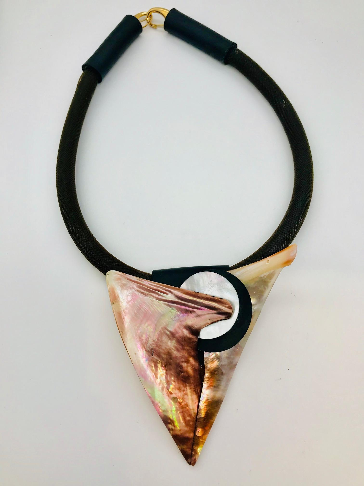 This Pendant Necklace is made from brown /gold nacre, which is eco–luxe and eco -friendly. This pendant is composed of two triangular shapes joined by two circular shapes made of white nacre and black rubber. The pendant is attached to a rubber tube